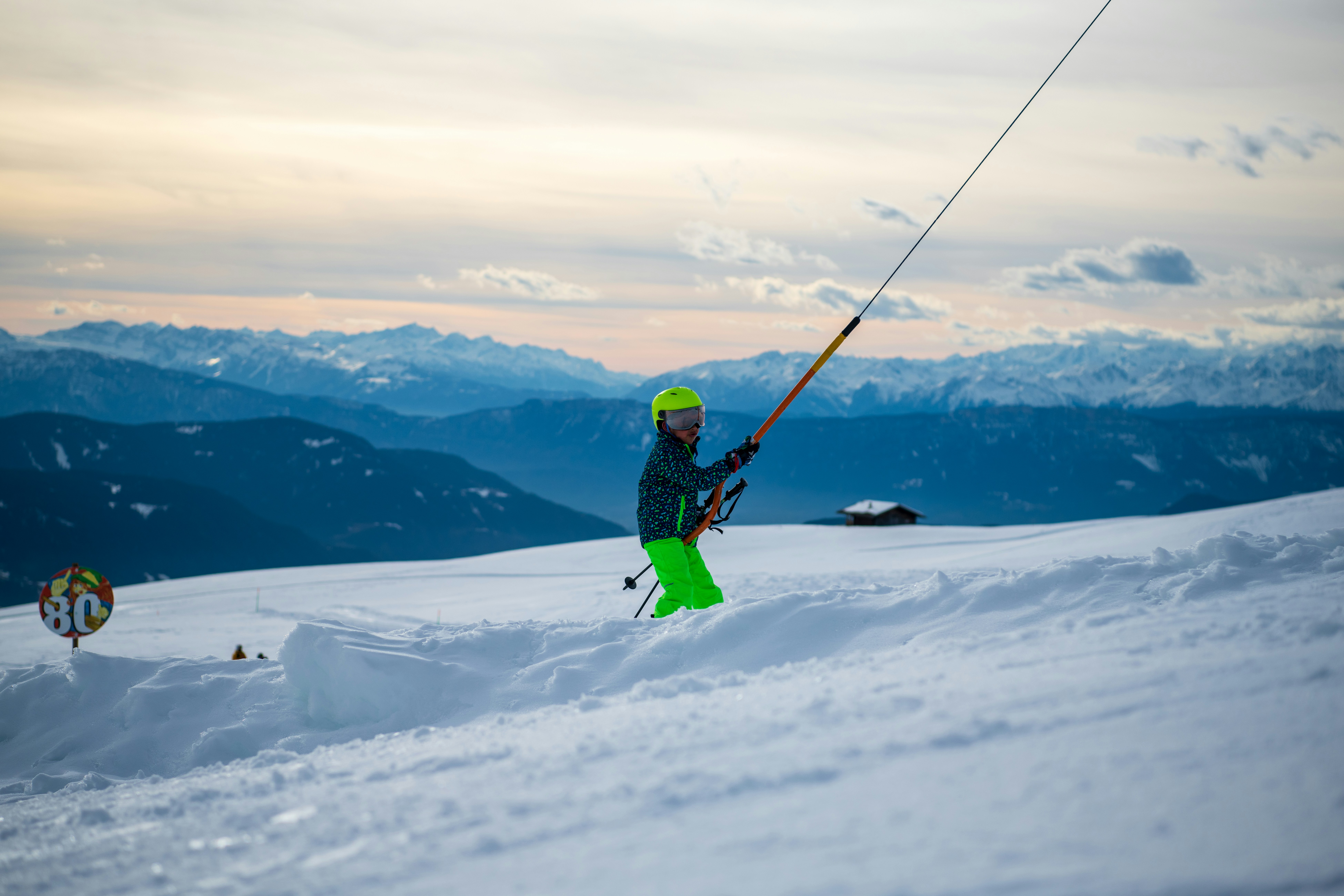 A skier in bright green pants holds ski lift pole