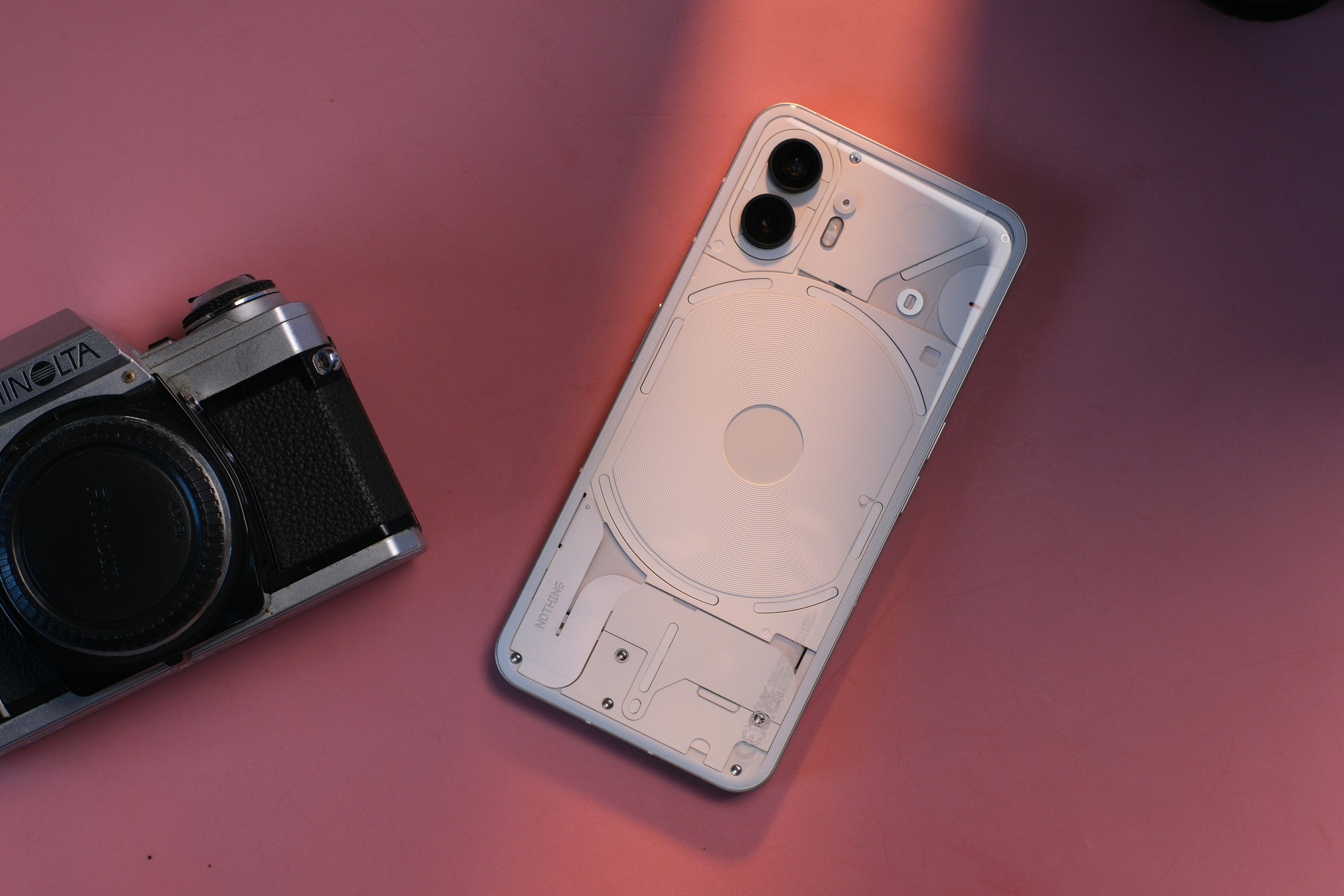 A white smartphone and vintage camera on a pink surface.