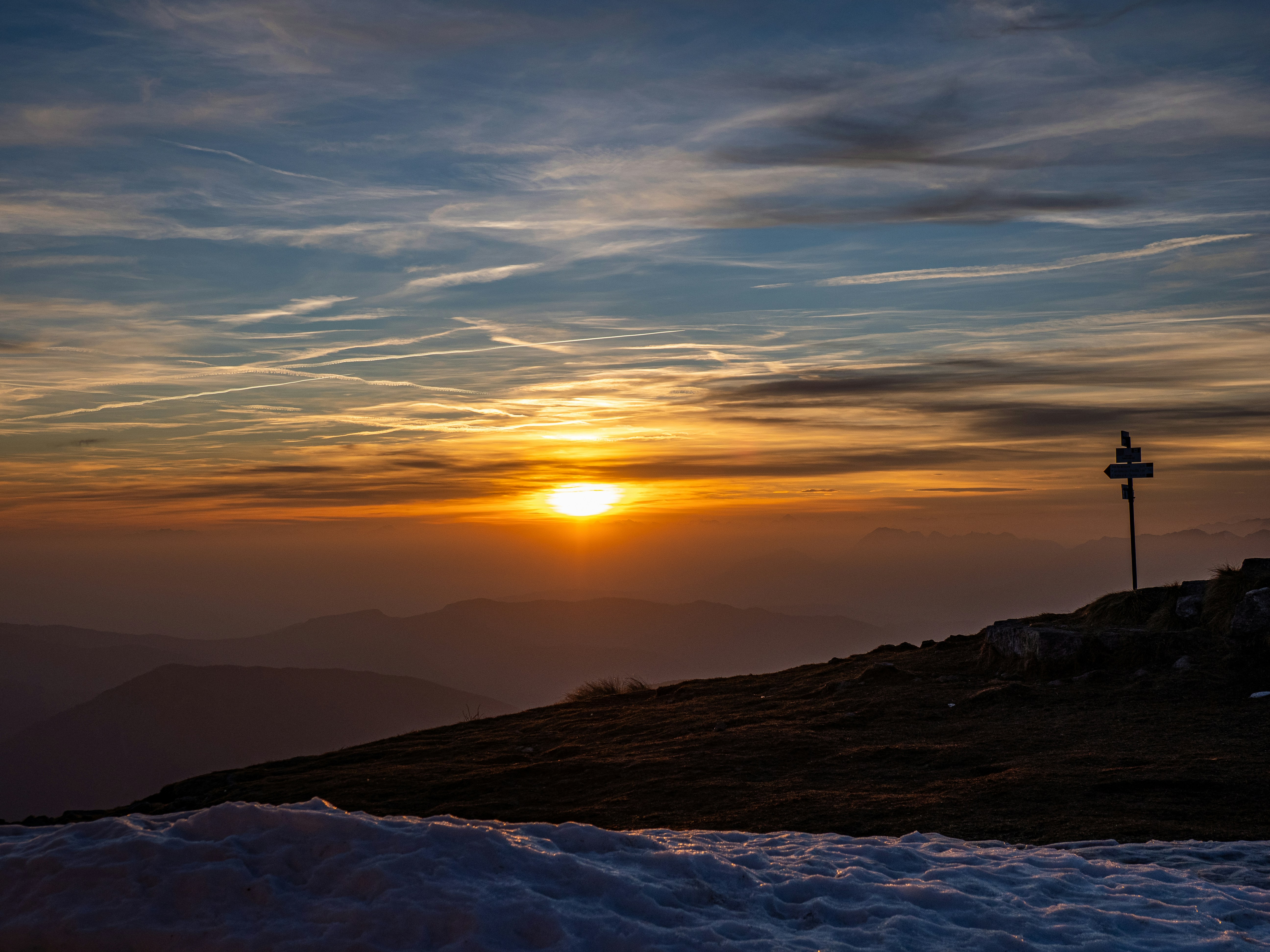 Sonnenuntergang über einem Bergrücken mit Wegweiser