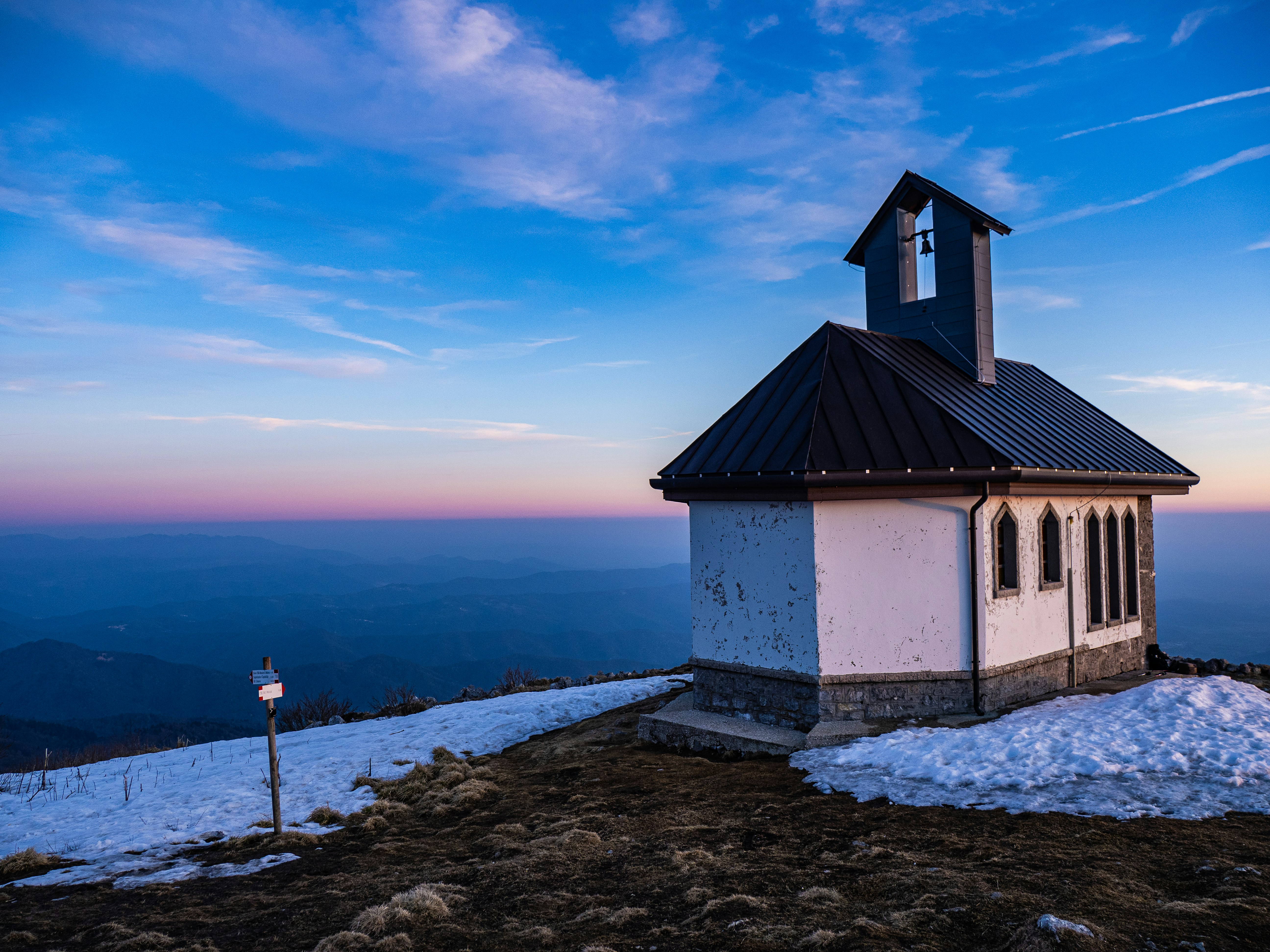Kleine Kapelle auf einem verschneiten Berggipfel bei Sonnenuntergang