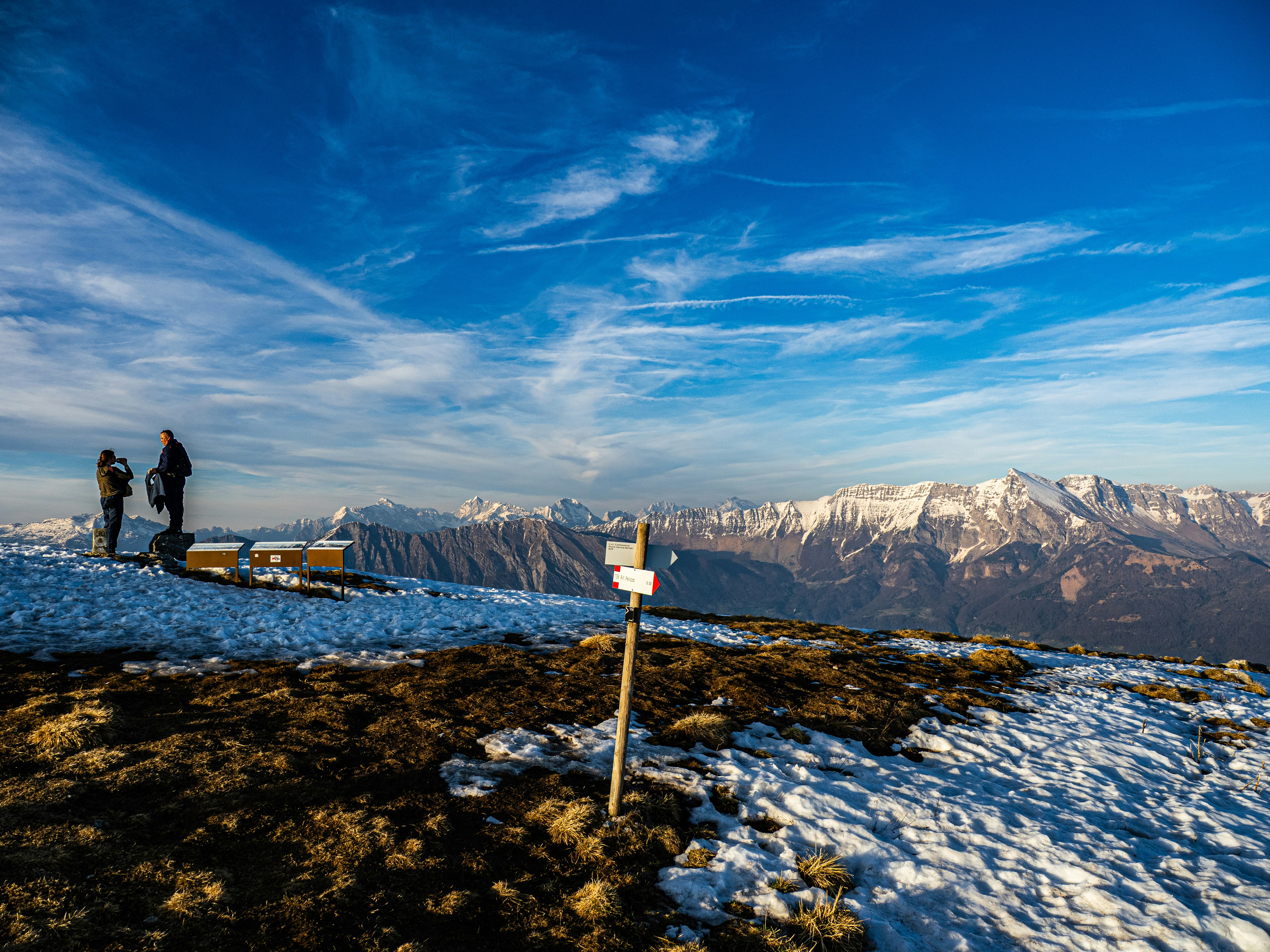 Zwei Wanderer auf einem verschneiten Berggipfel mit weit entfernten Gebirgszügen.