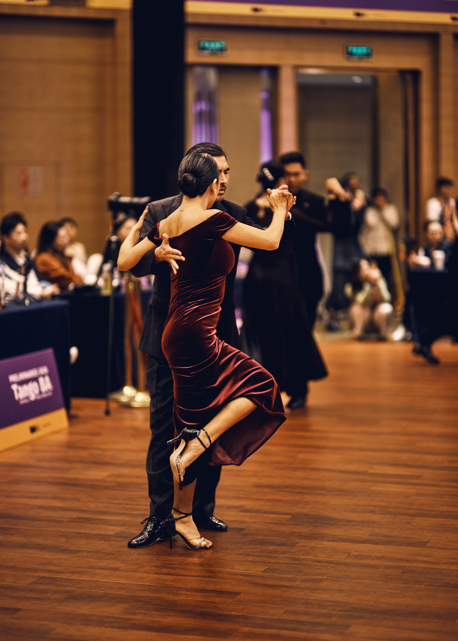 A couple dances tango on a wooden floor.
