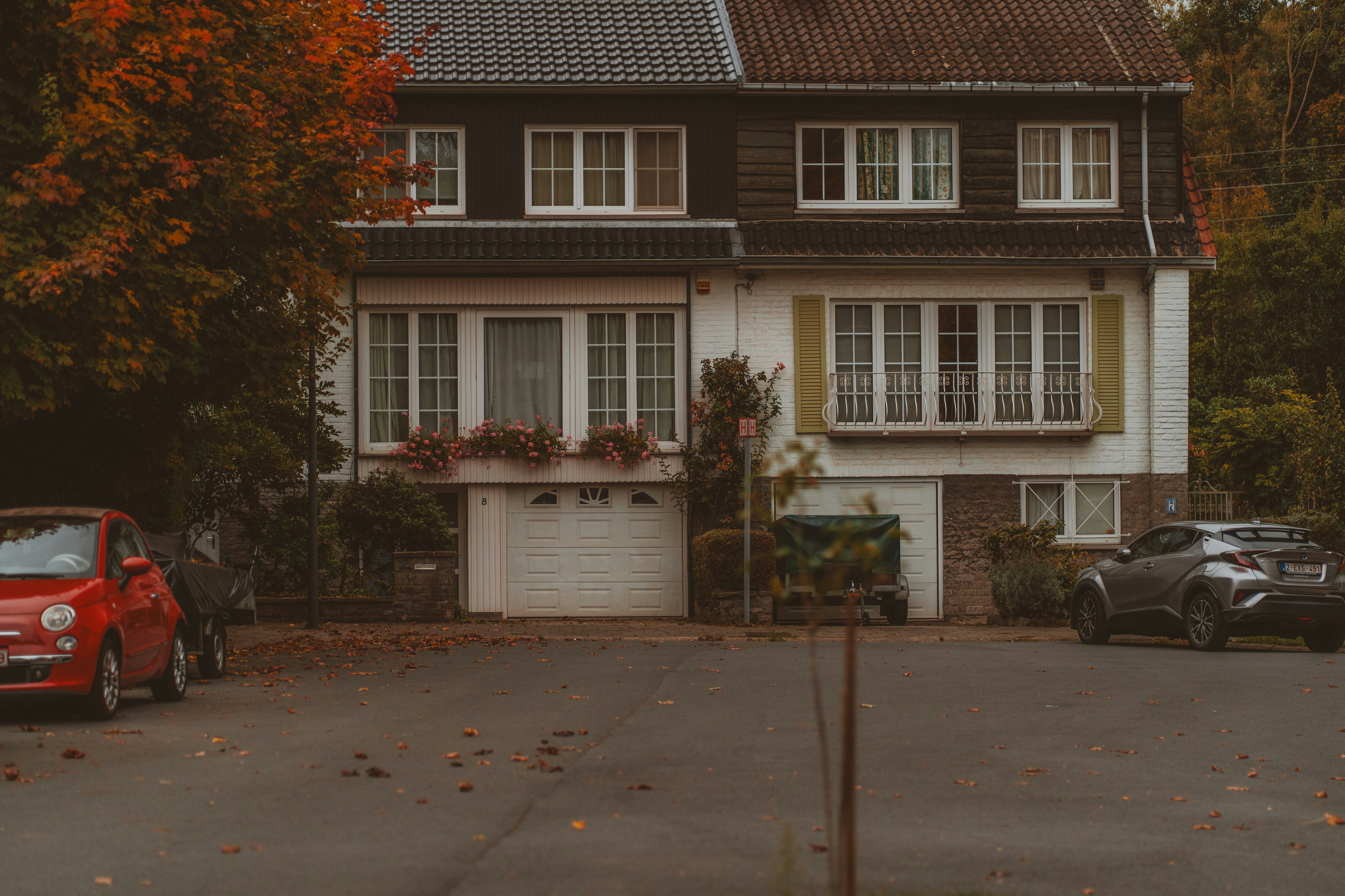 Two cars parked outside a suburban house in autumn.