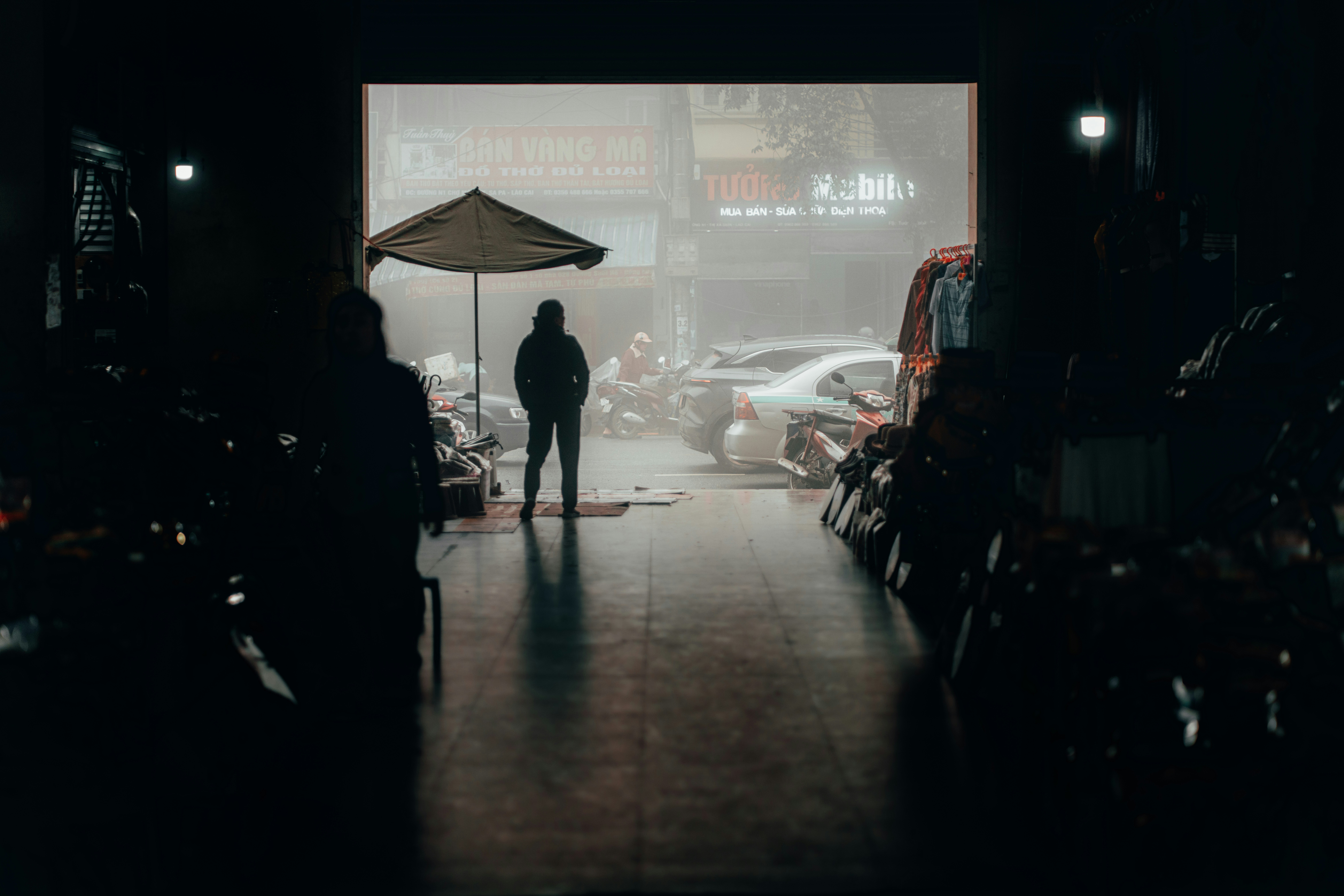 A lone figure stands under an umbrella in the rain