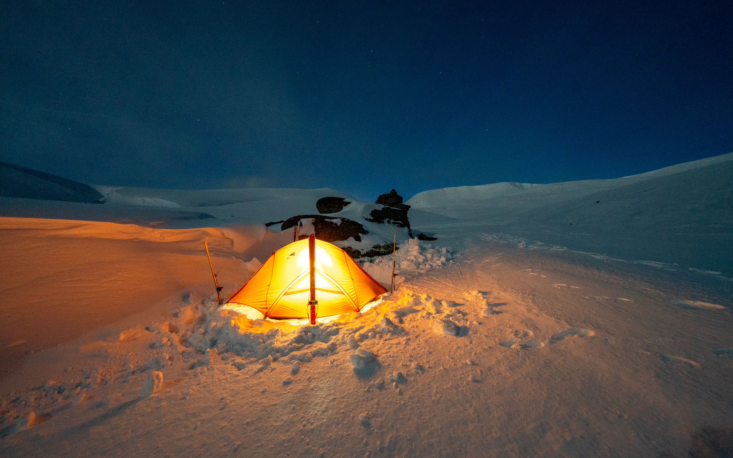 A glowing tent on a snowy slope at night under a starry sky