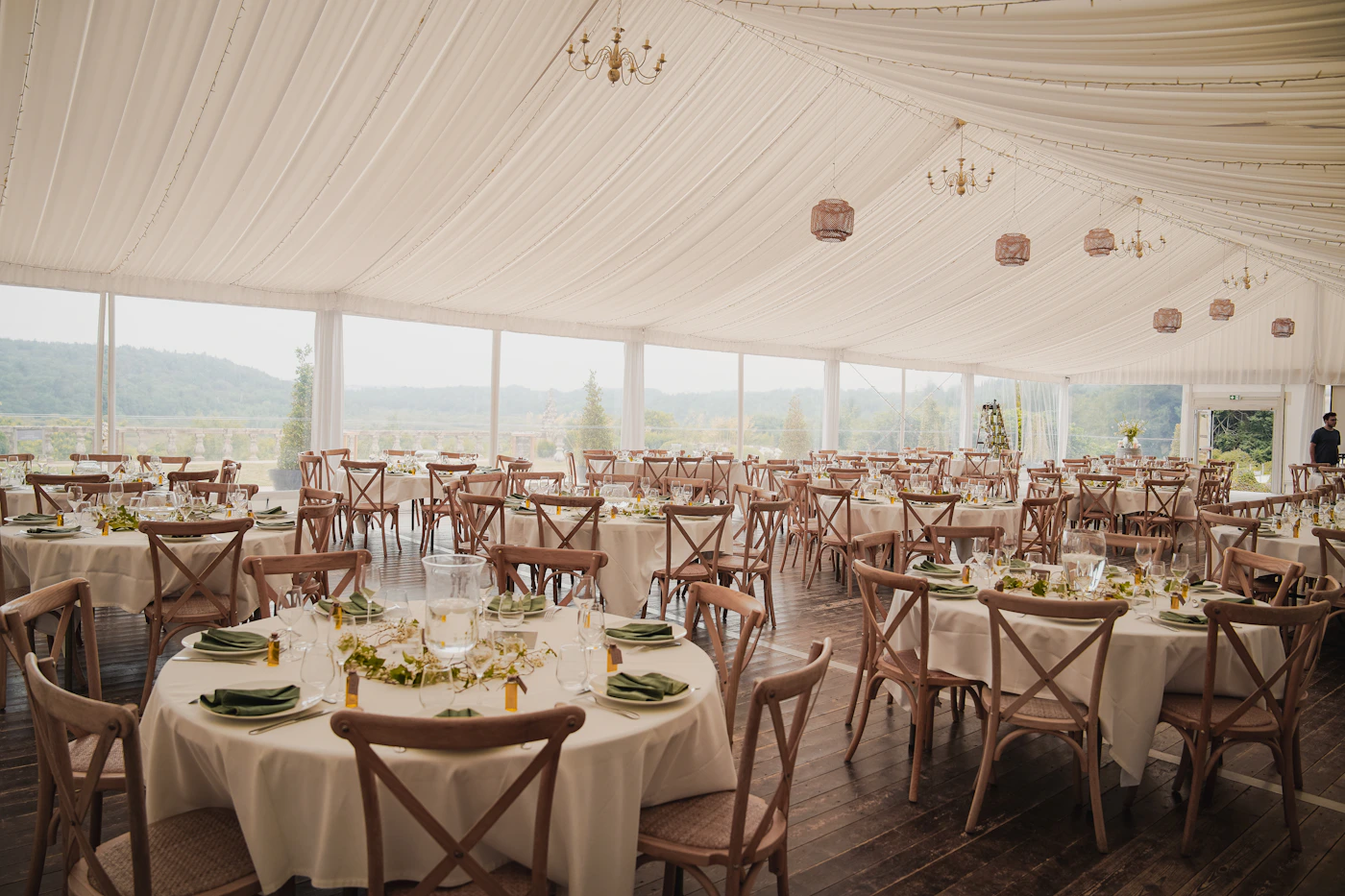 An elegant outdoor wedding reception tent with round dining tables set with white linens and formal floral centrepieces under a white reception canopy for a destination wedding dinner