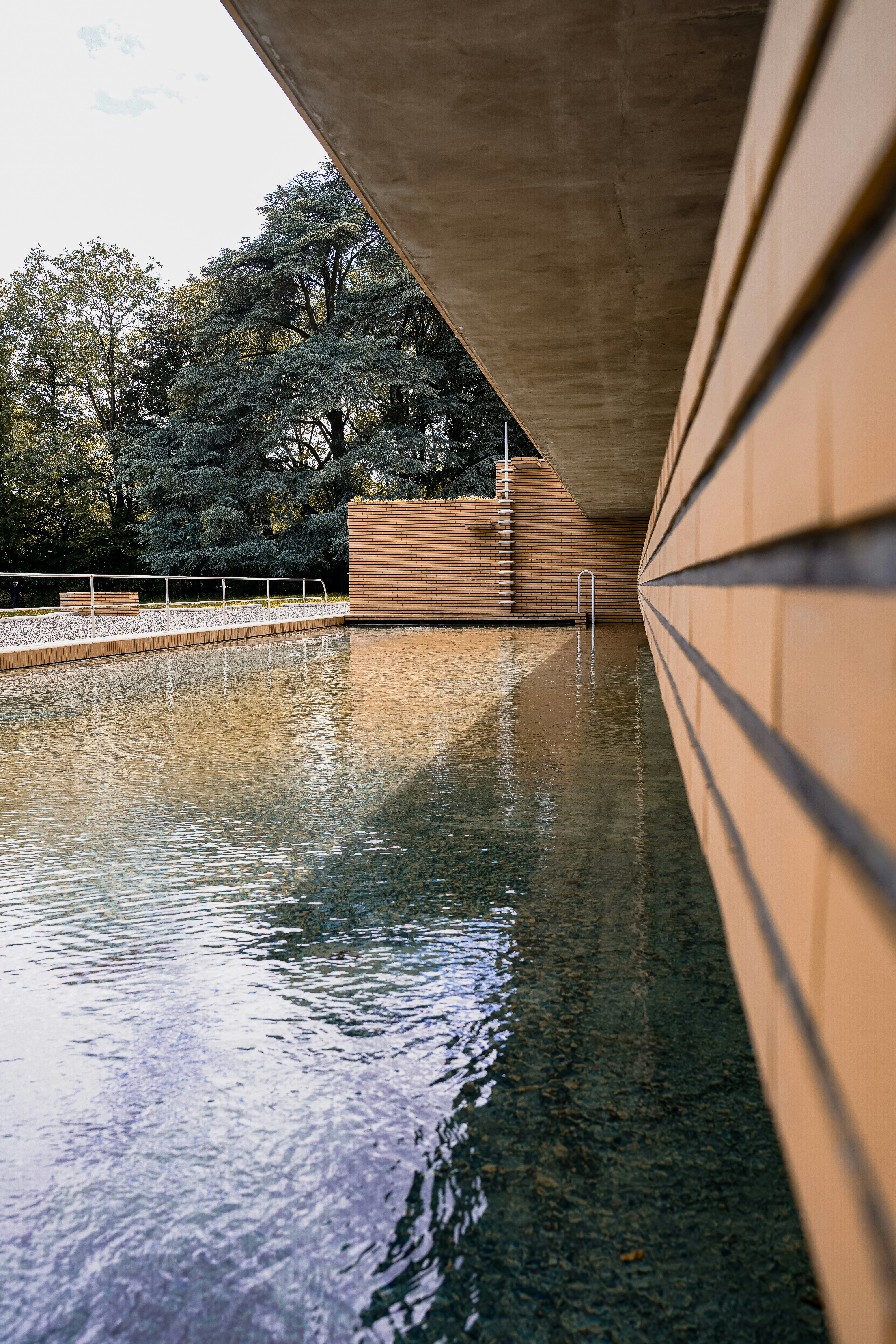 Modernes Gebäude mit reflektierendem Schwimmbecken und Bäumen.