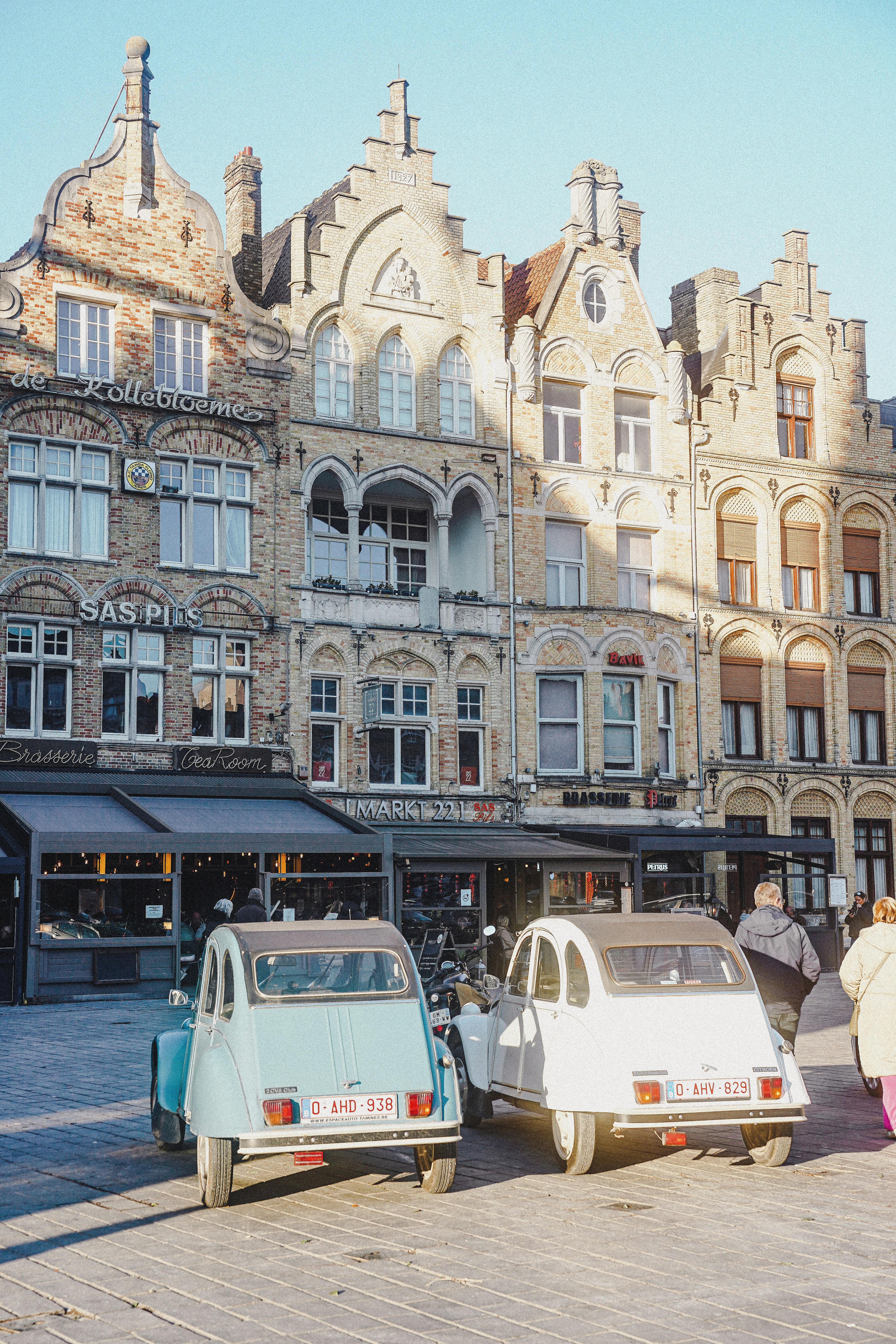 Zwei Oldtimer, die vor alten Gebäuden geparkt sind.