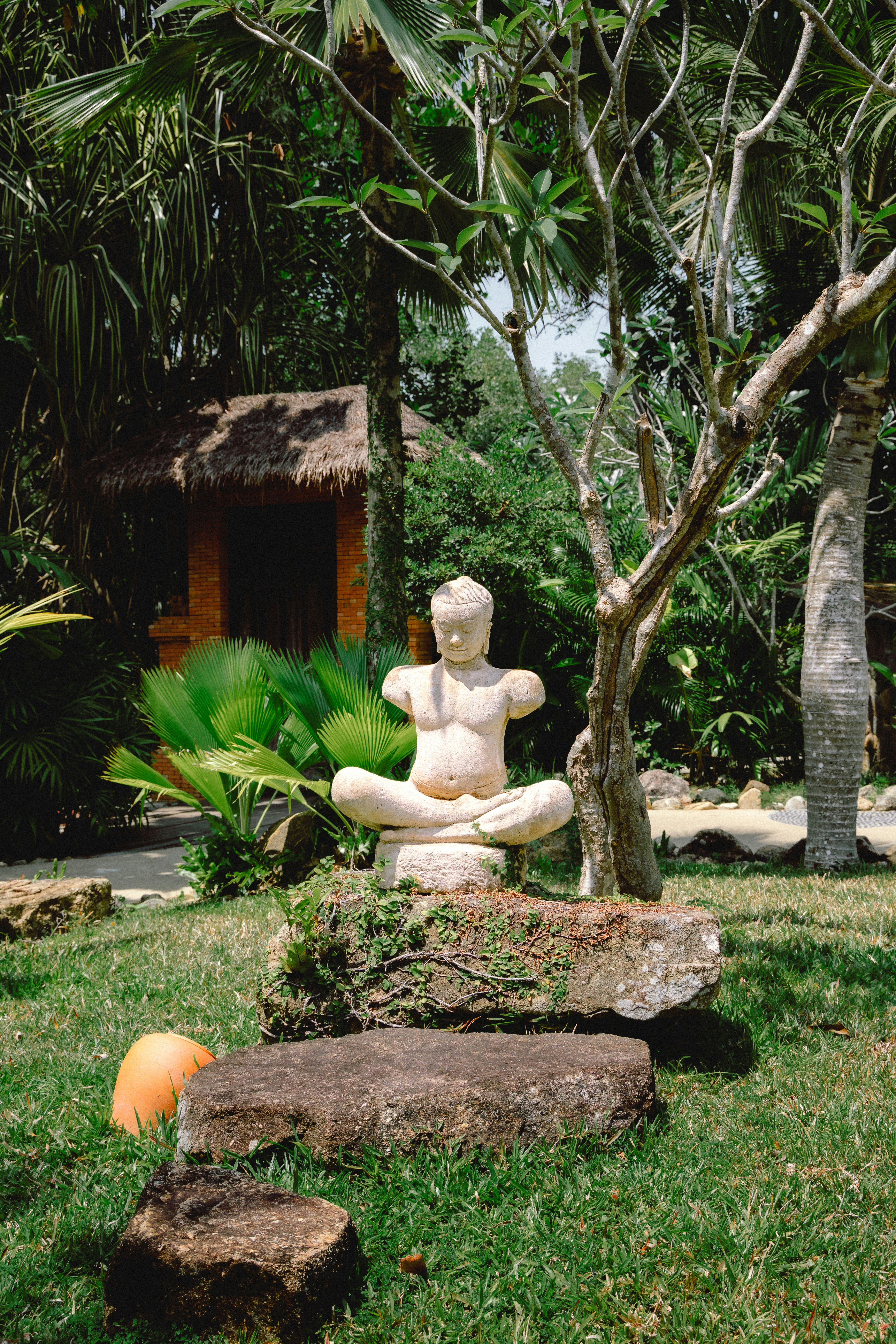 Stone statue of a person meditating in a garden.