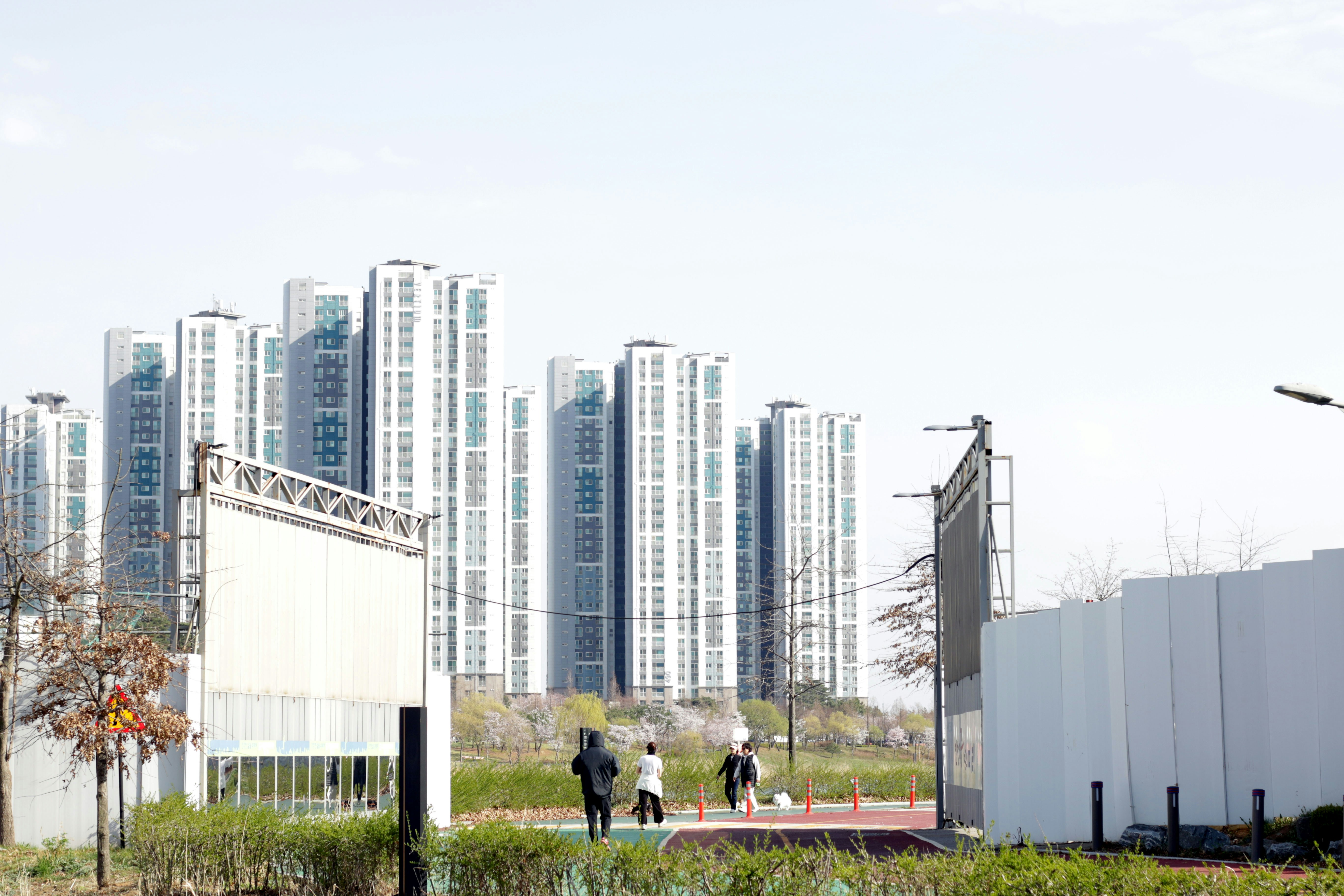 Apartment buildings rise behind a park with people walking.