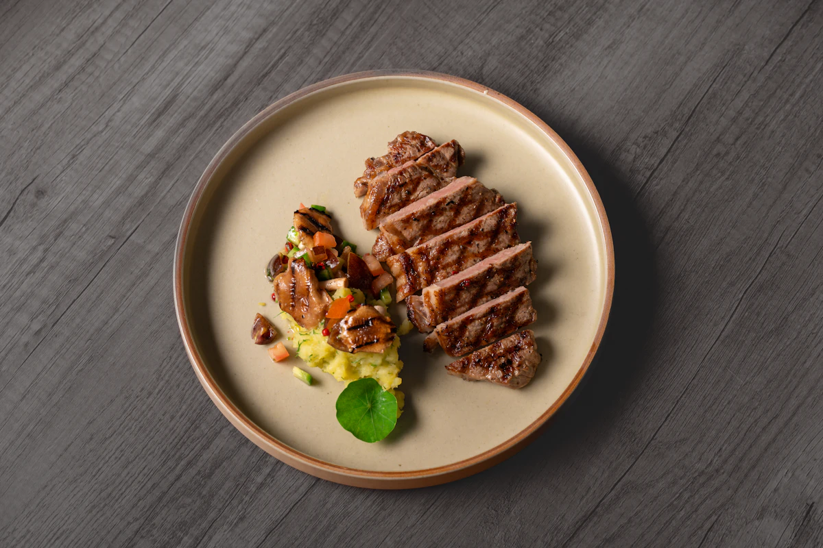 A plate of sliced grilled steak with a small side of vegetables