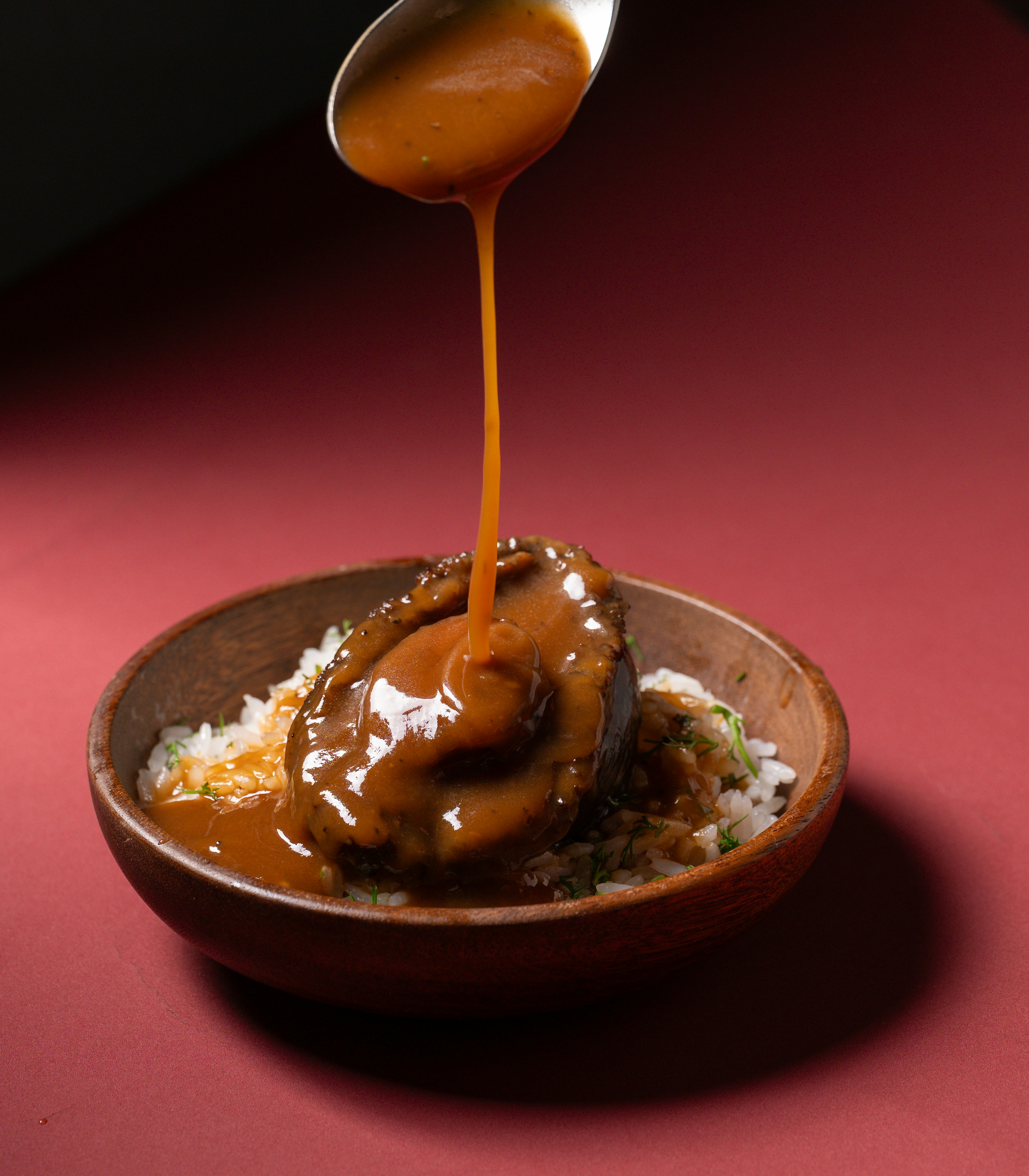 Salsa vertida sobre abulón y arroz en un bol.