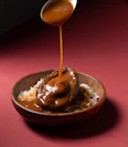 Sauce being poured over abalone and rice in a bowl.