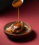 Sauce being poured over abalone and rice in a bowl.