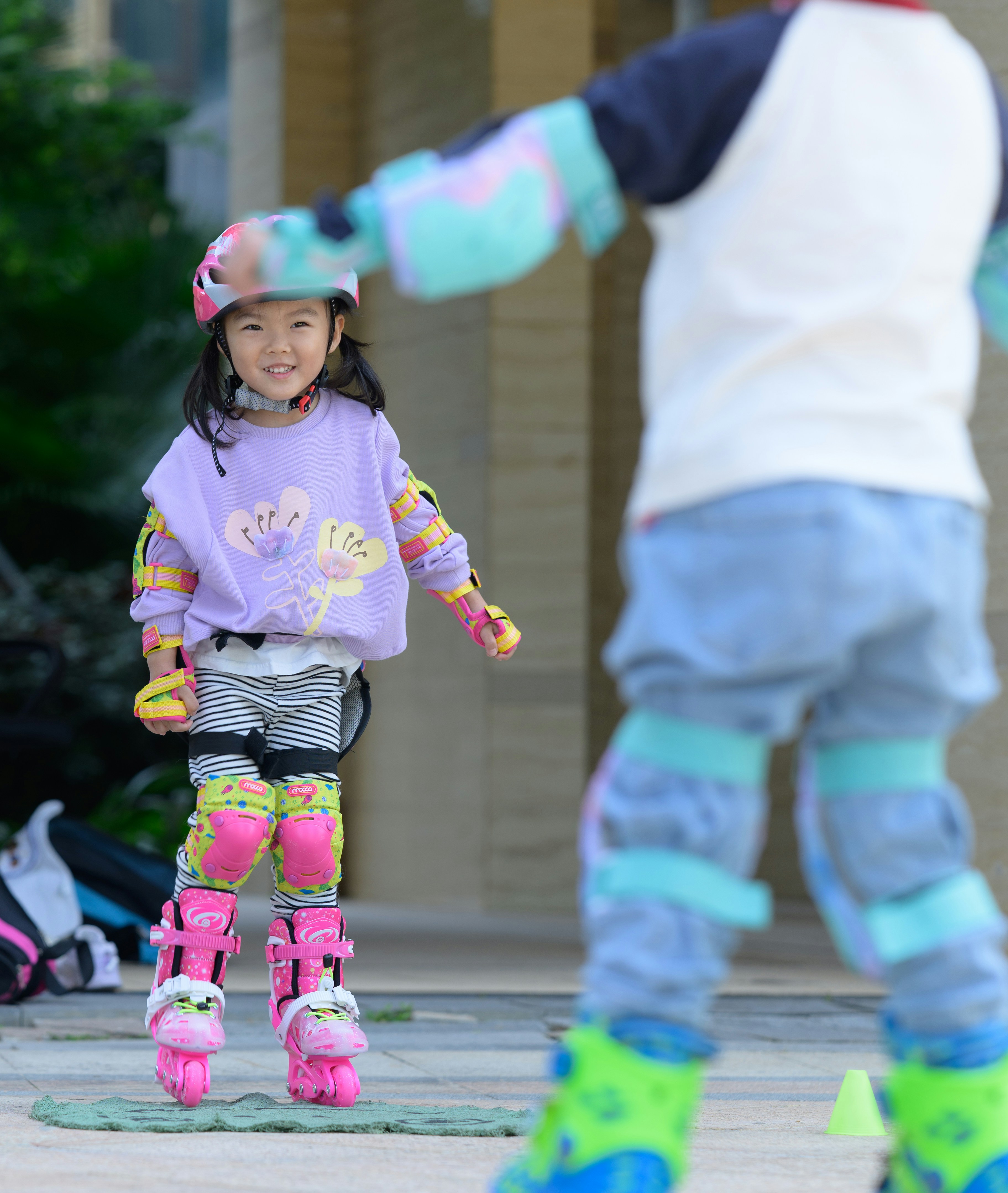Two children rollerblading outdoors with protective gear.