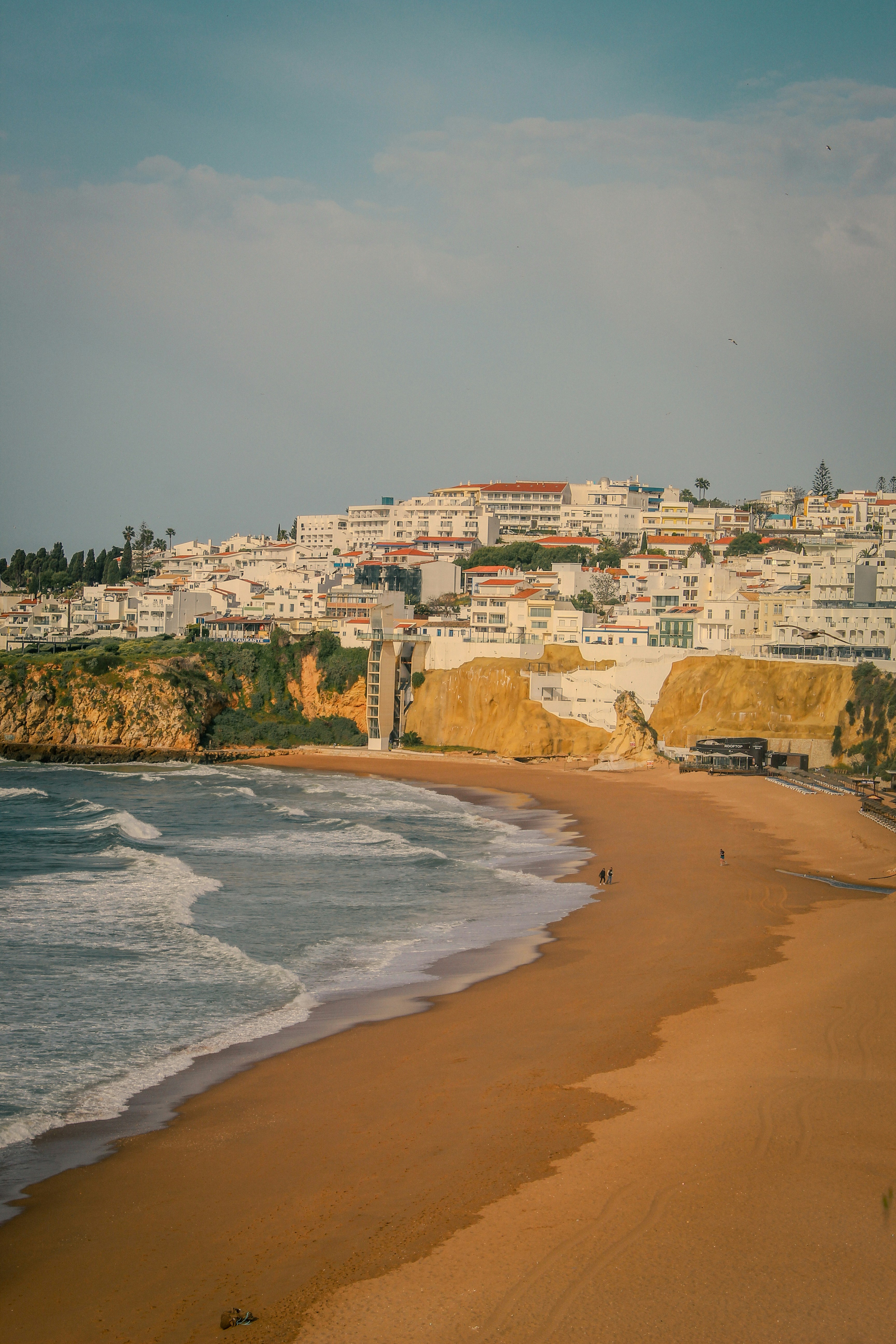 Ville côtière avec des bâtiments blancs surplombant une plage de sable.