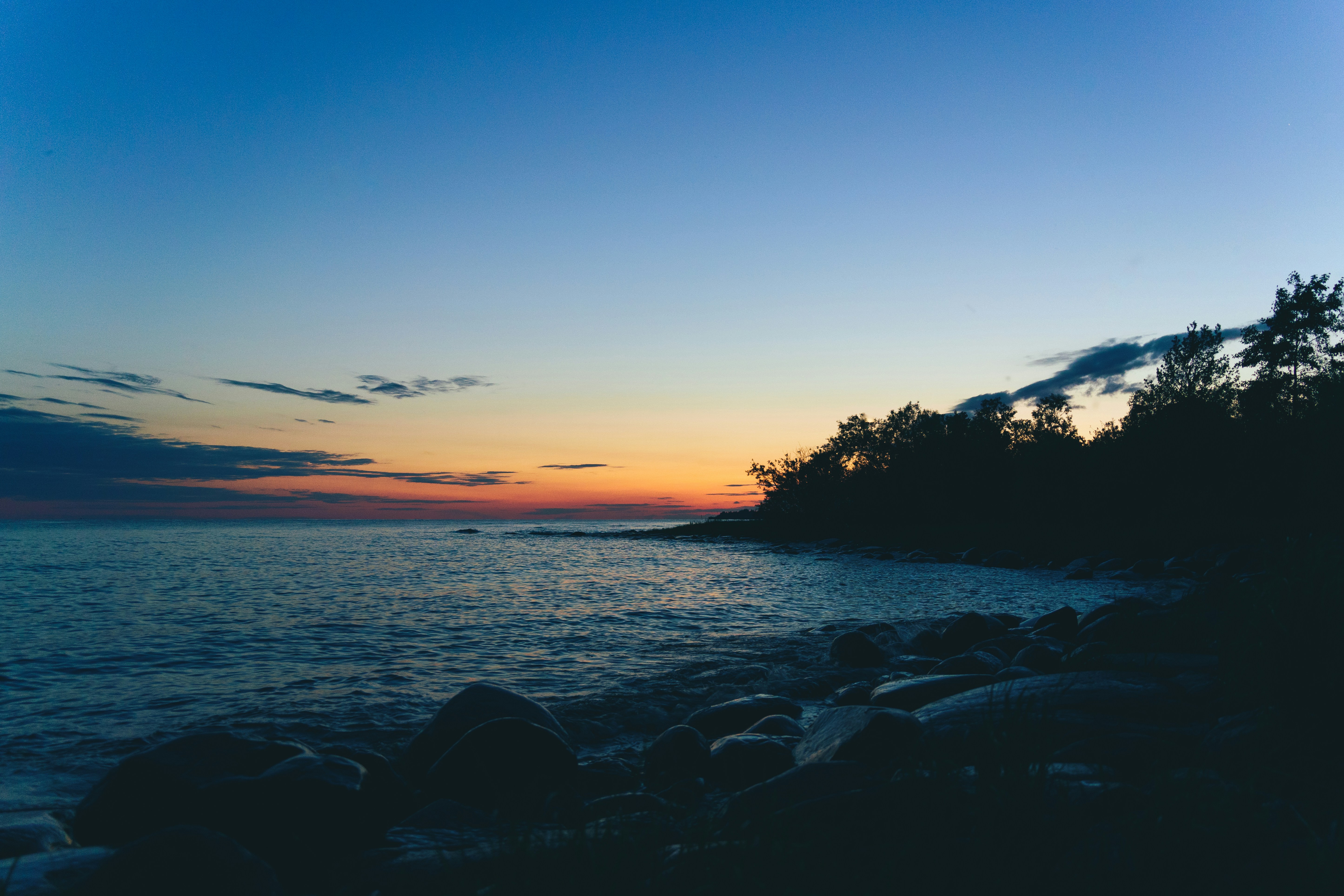 Sunset over a calm ocean with rocky shore.