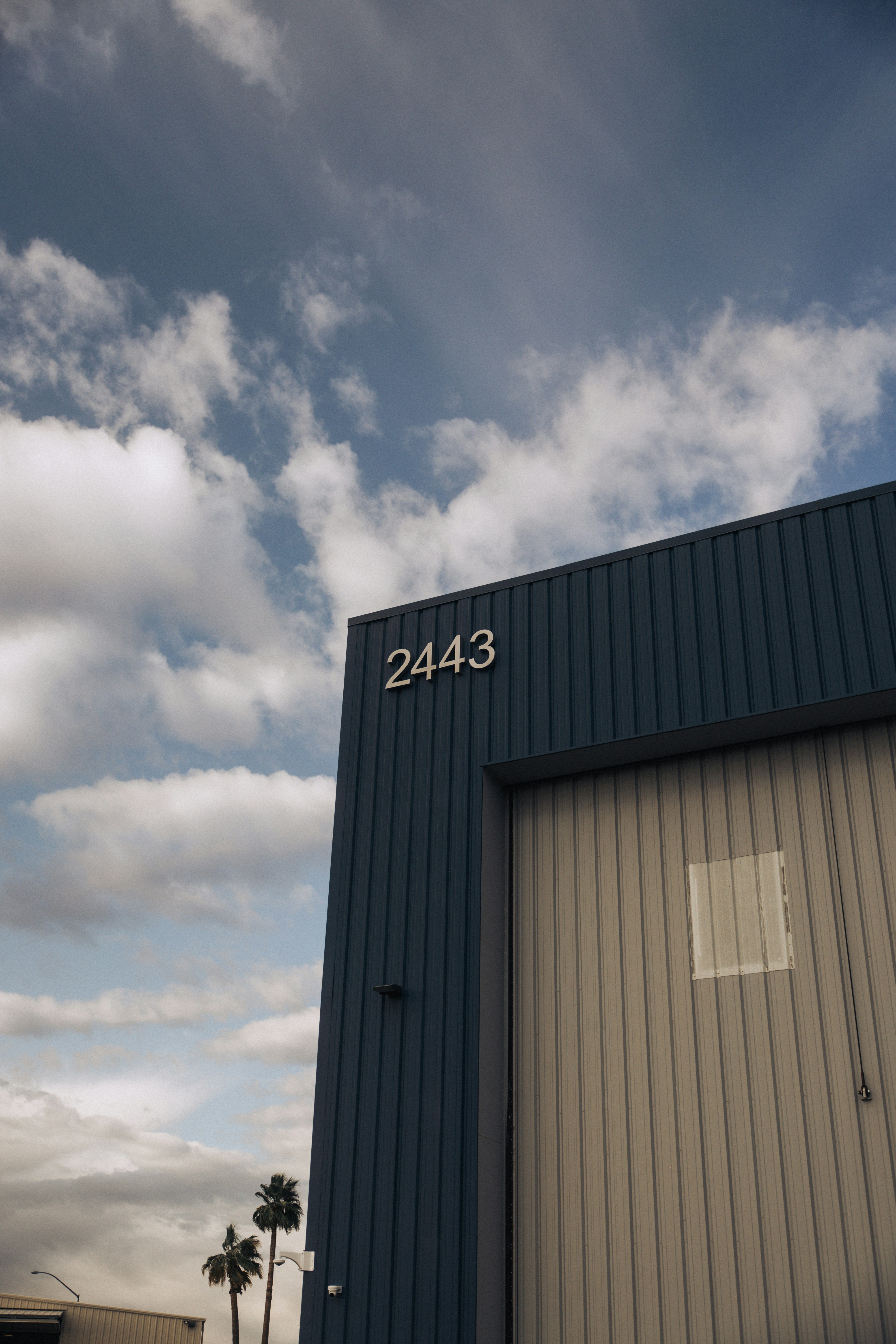 Blue industrial building with large garage door under sky.