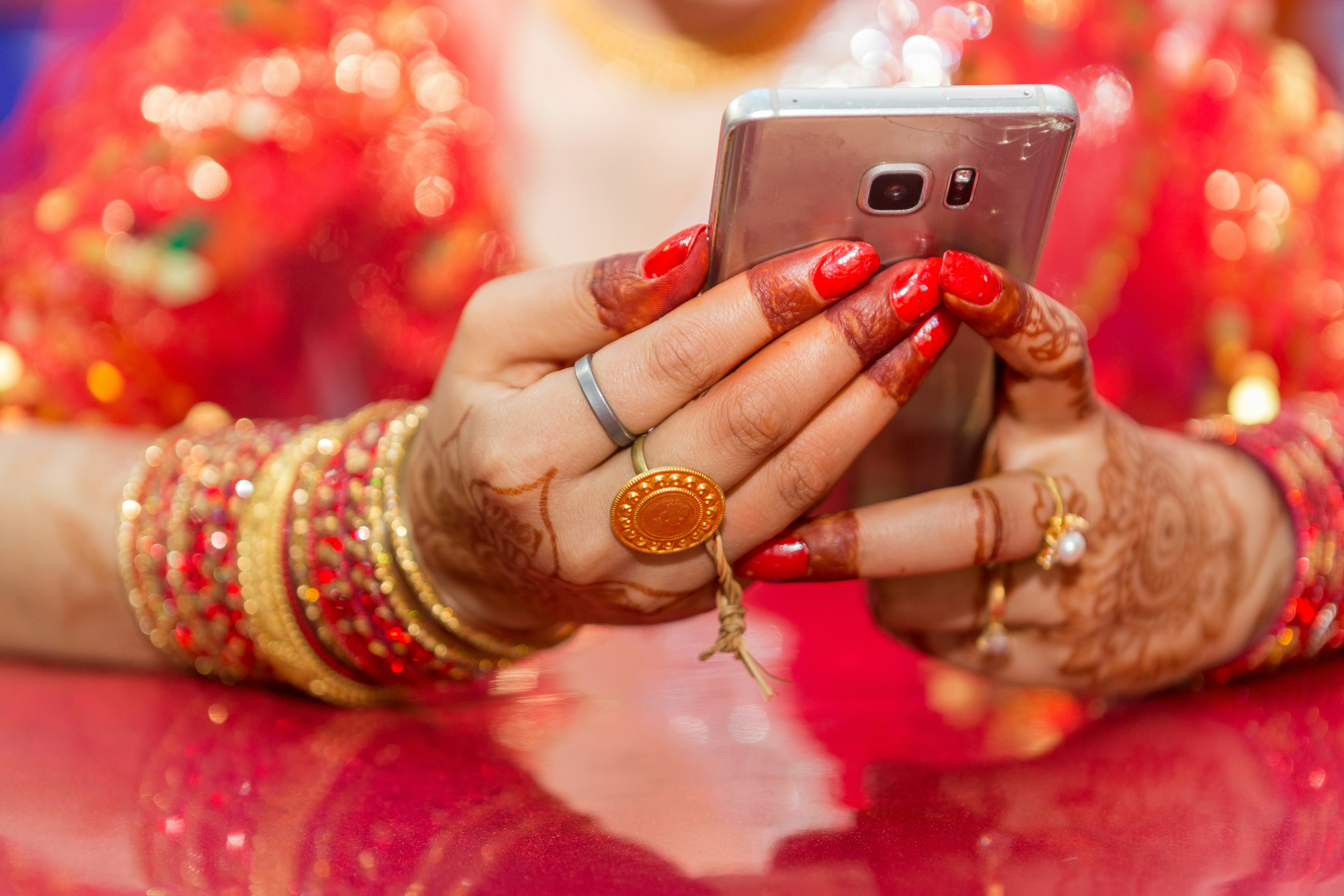 A close-up shot of a smartphone screen displaying real-time gold prices in different Indian cities with varying carats, blurred background of a jewelry shop.