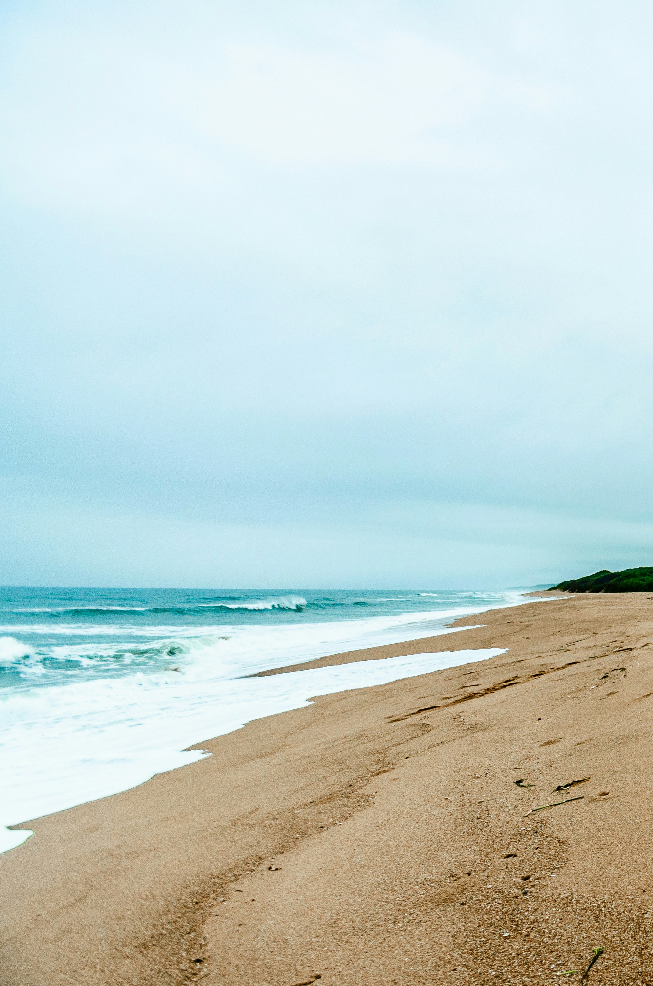 Spiaggia sabbiosa con onde dell'oceano sotto un cielo nuvoloso.