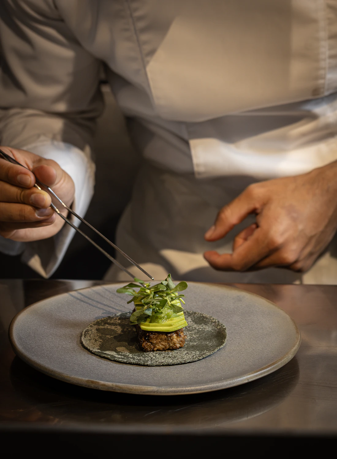 Manos de chef colocando hojas frescas sobre un plato con pinzas