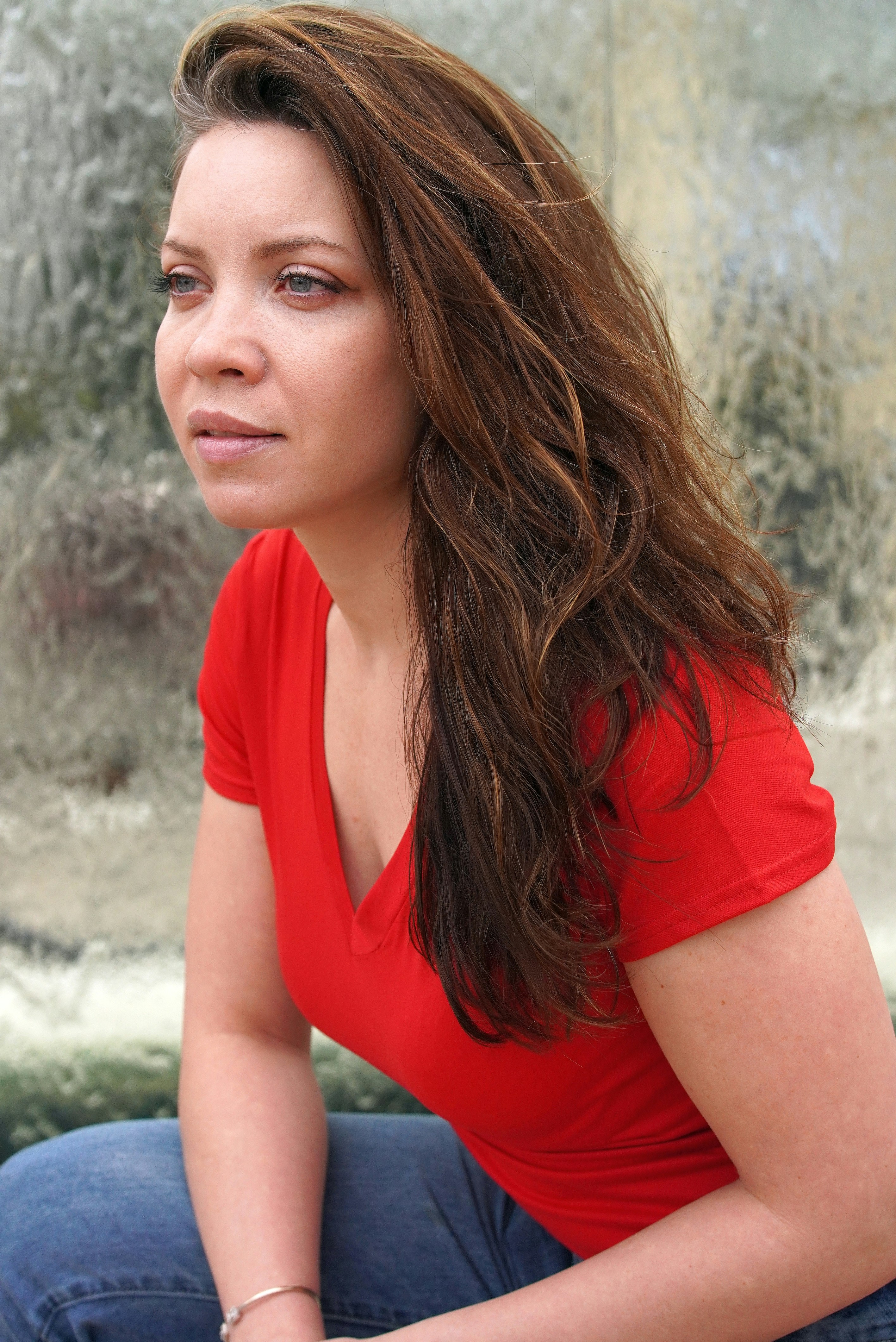 Une femme en chemise rouge et jean détourne le regard.