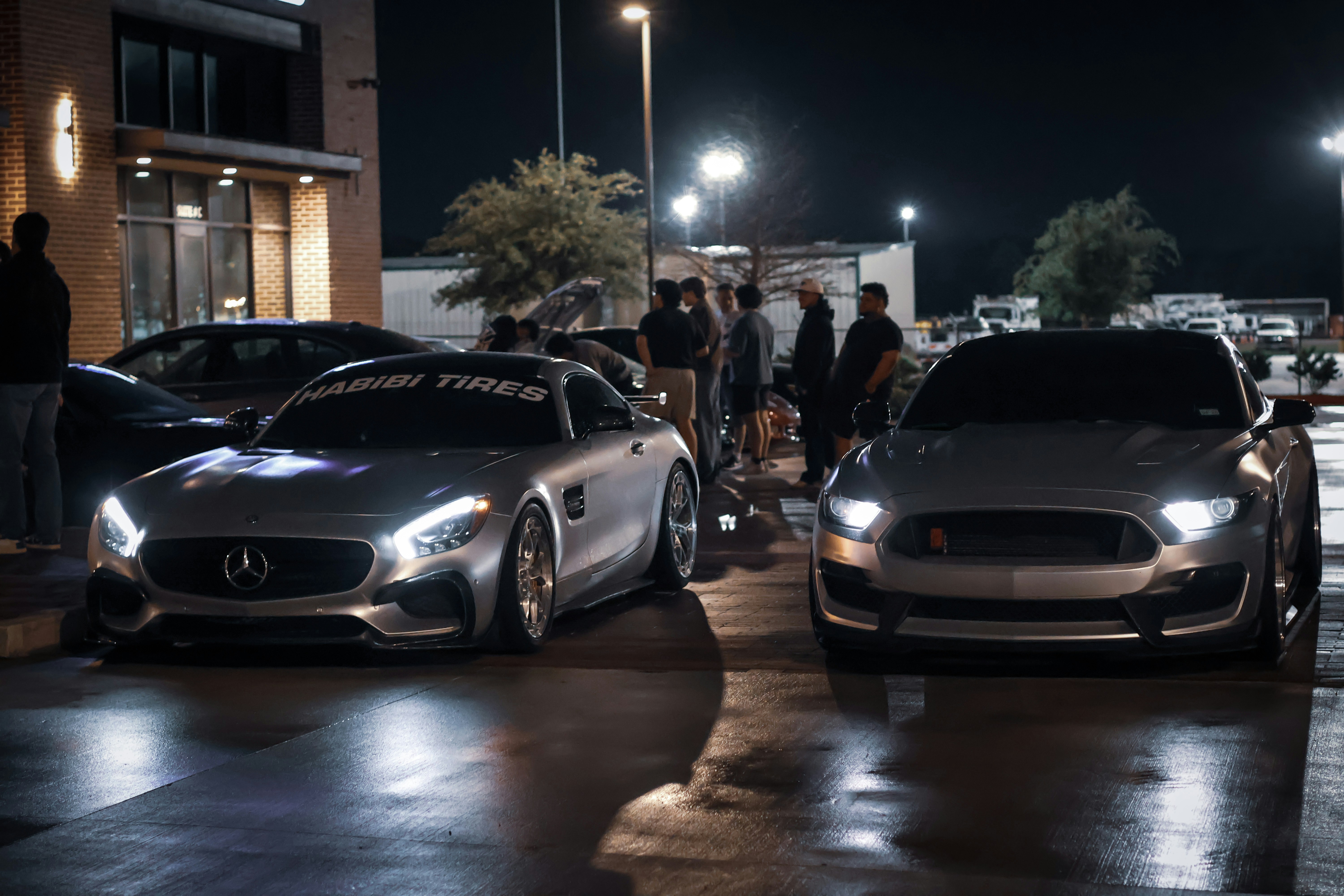 Two sports cars parked at night with people around