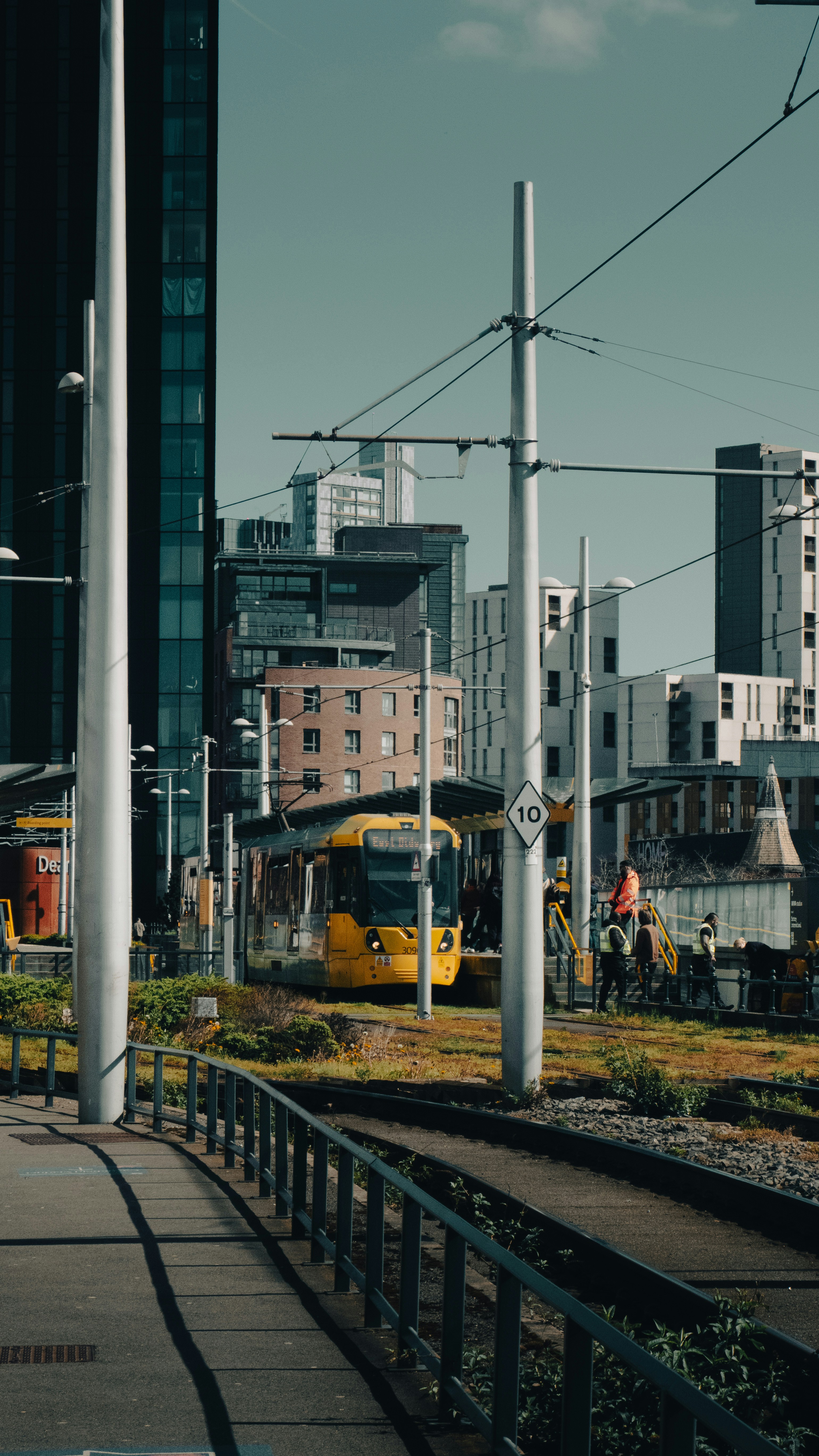 Yellow tram at station with modern buildings in background.