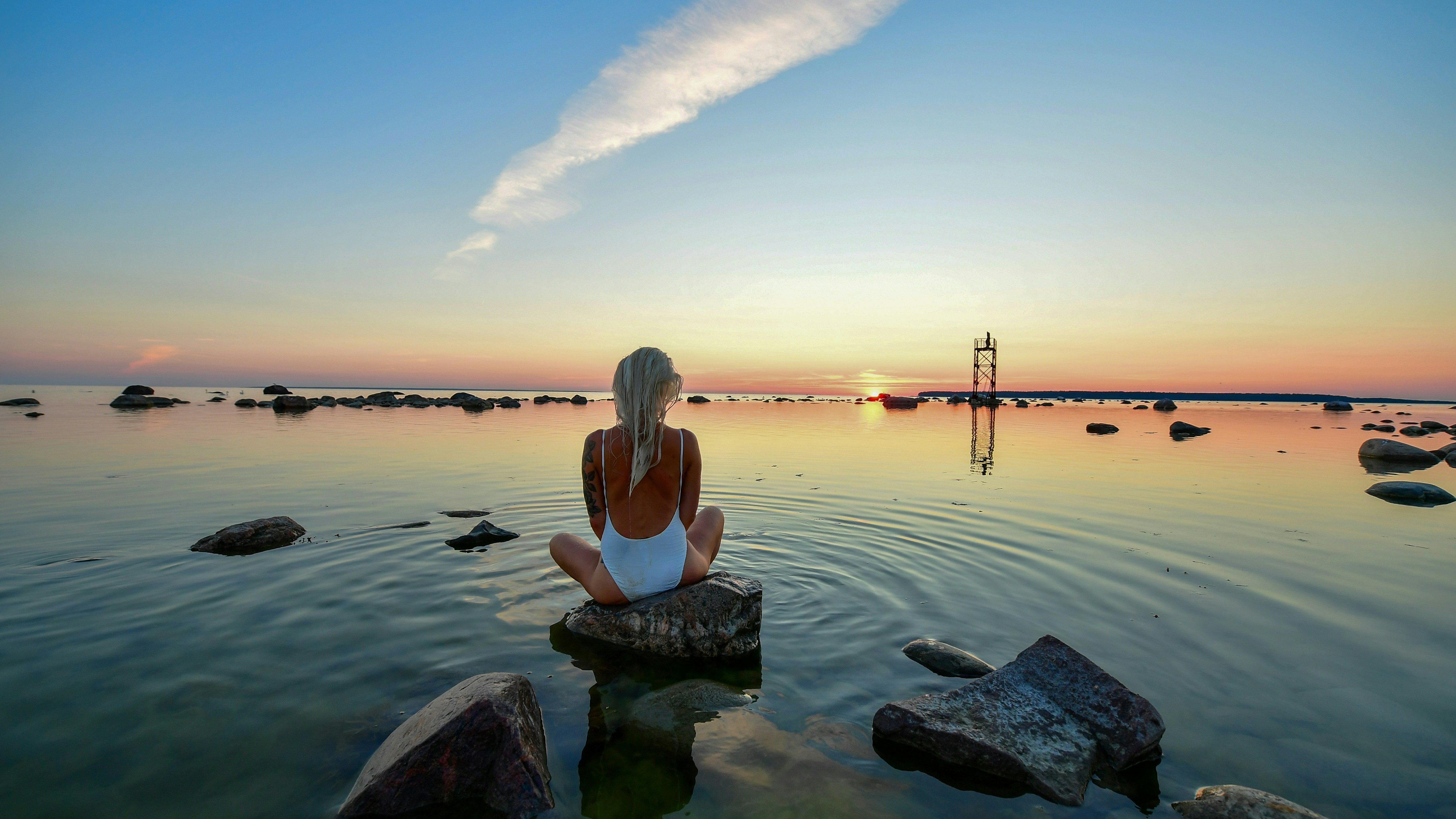 Woman sitting on rock by the calm ocean at sunset
