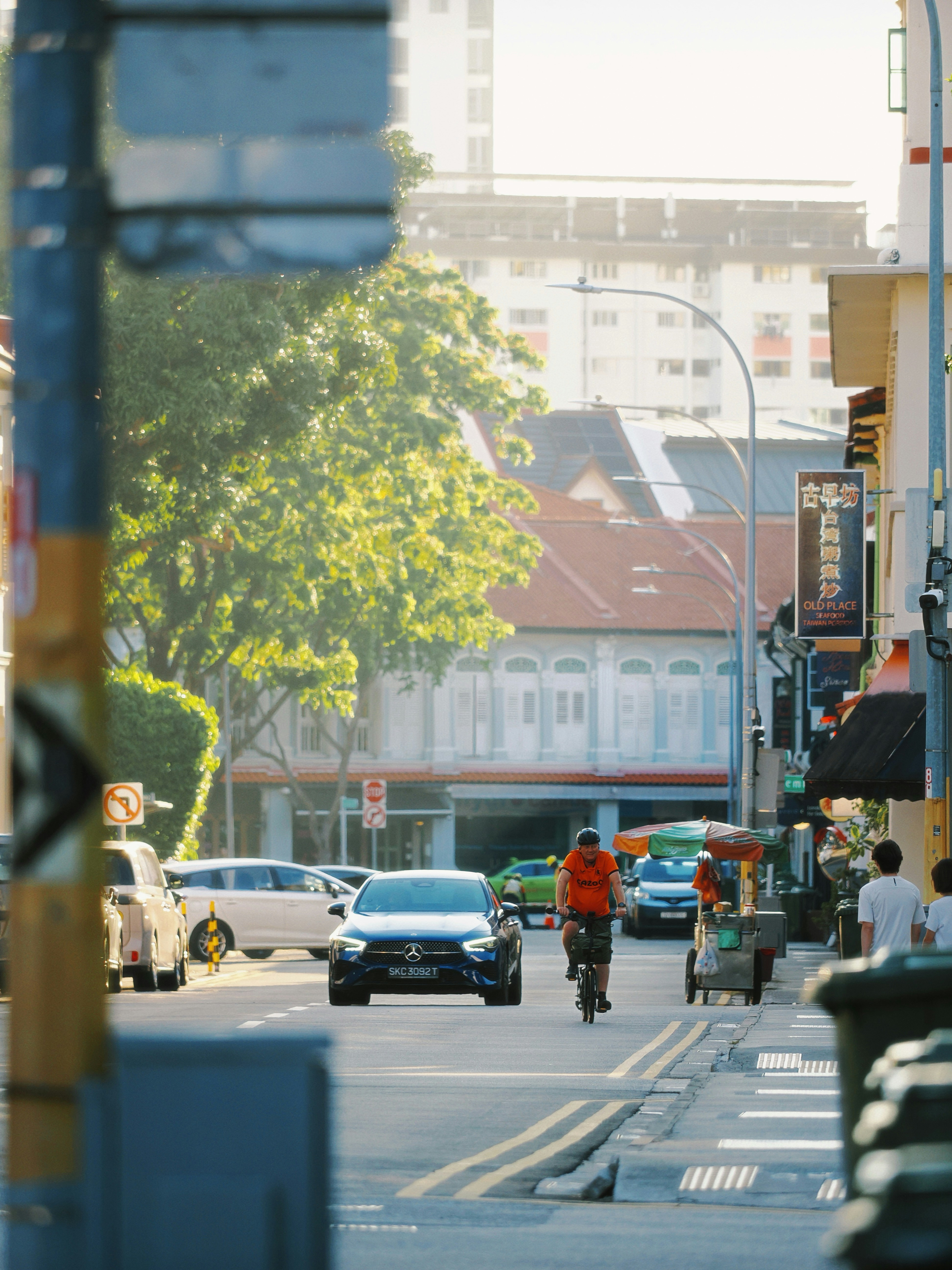 Man cycles down a street with cars and buildings.