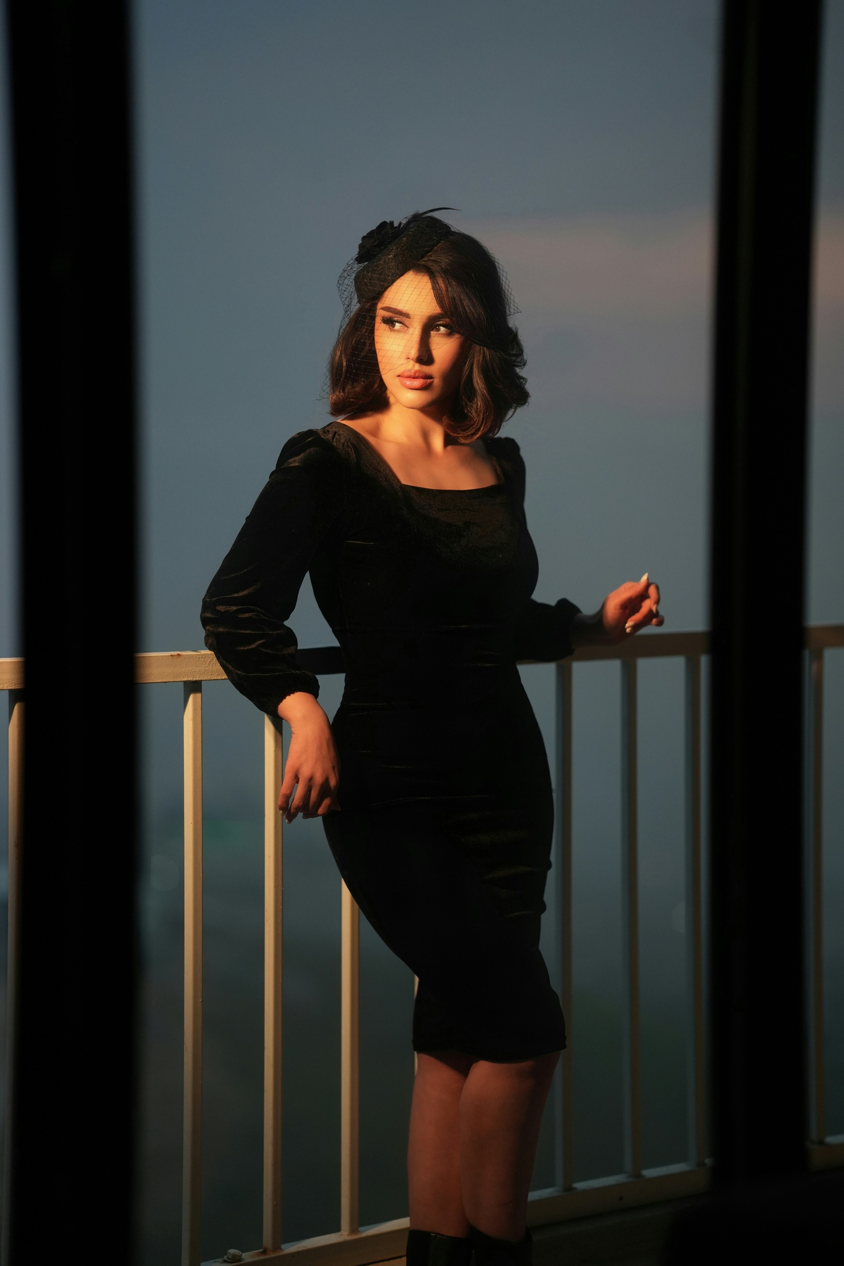 Elegant woman in black dress on balcony at sunset
