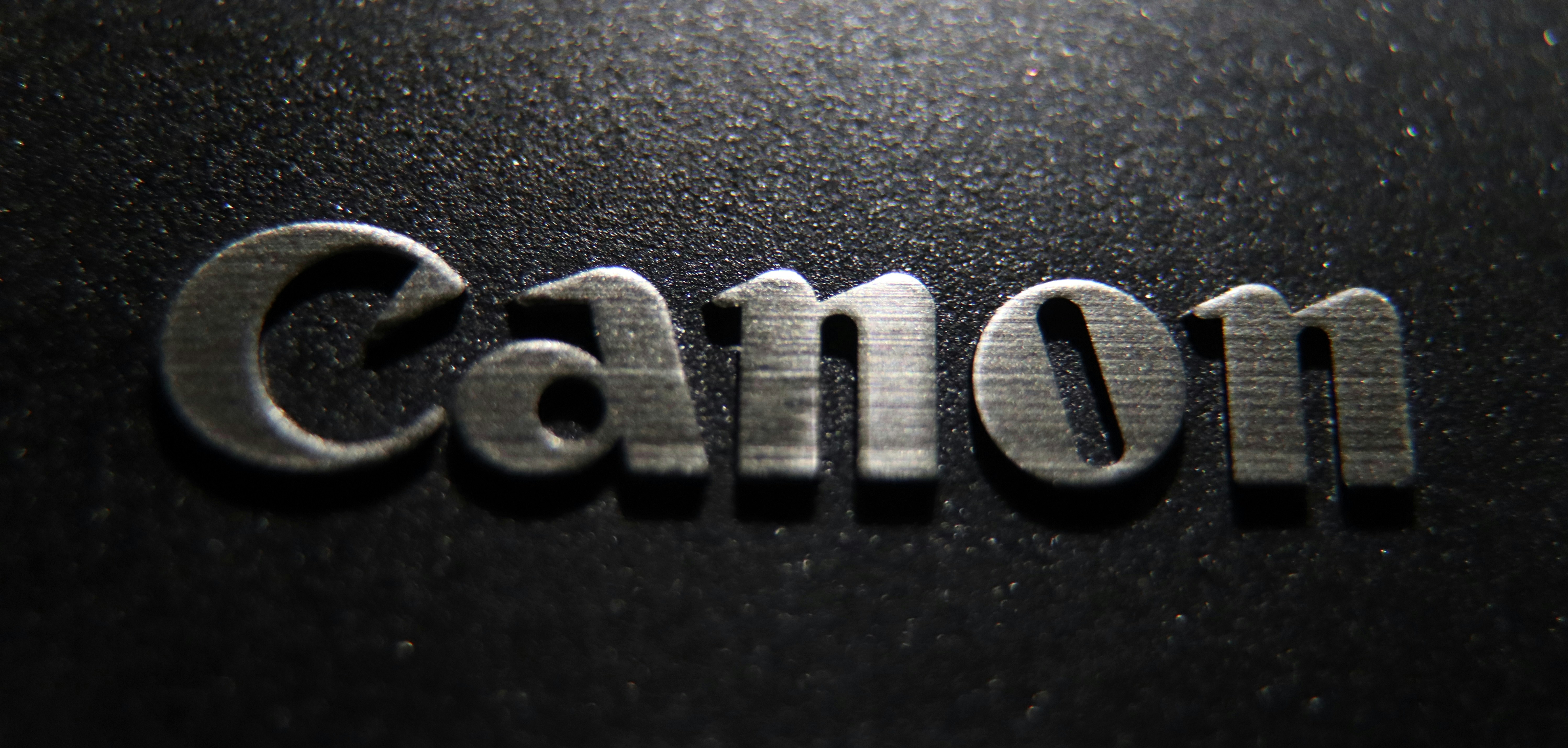 暗い表面に金属製のキャノンロゴのクローズアップ。