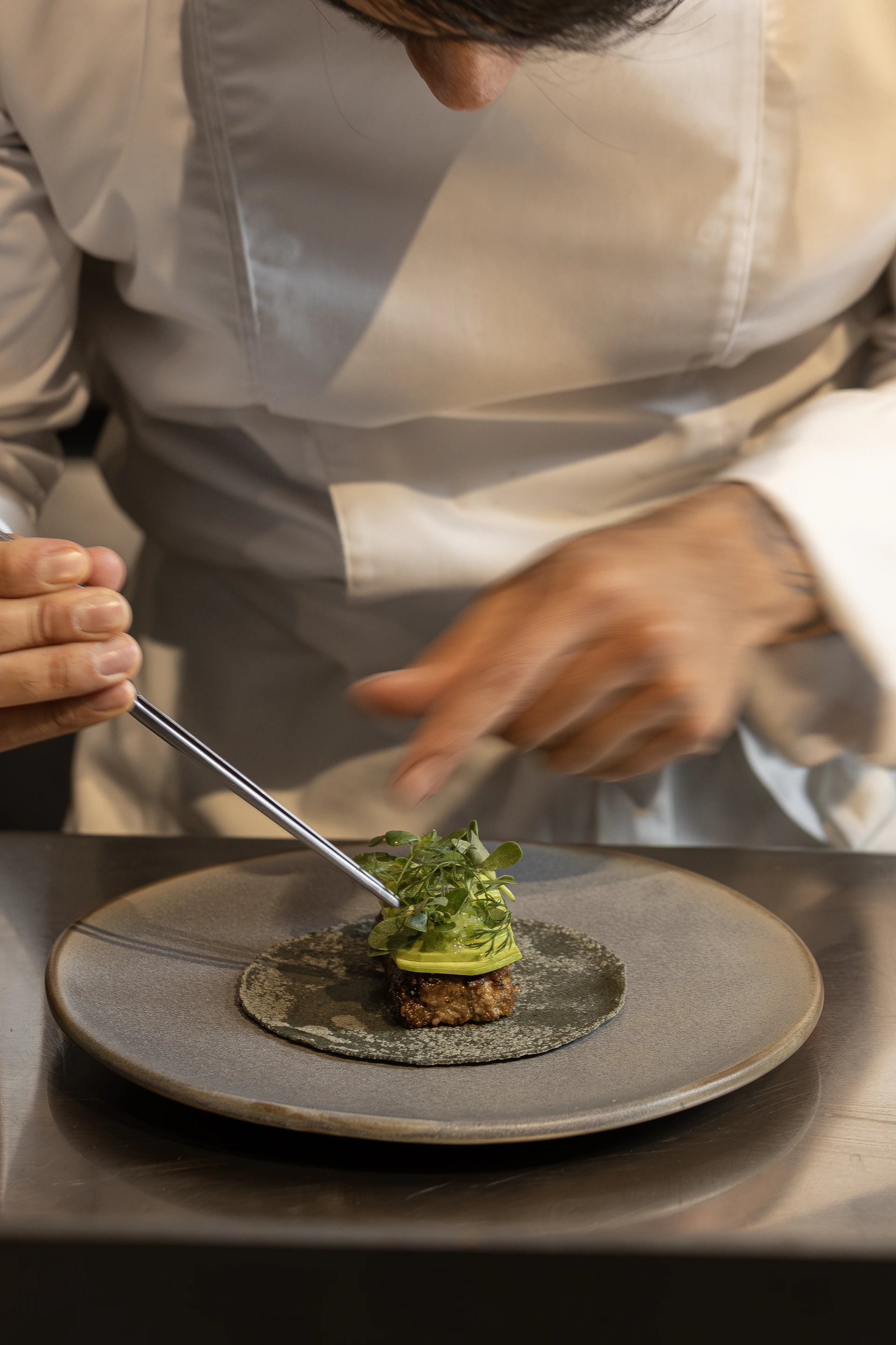 Chef carefully plating a gourmet dish with tweezers
