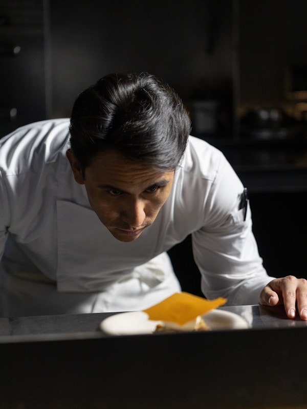 Chef intently working on a dish with orange garnish, precise hand movements over a white plate.
