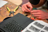 Hands wiring electronics with tools and laptop nearby
