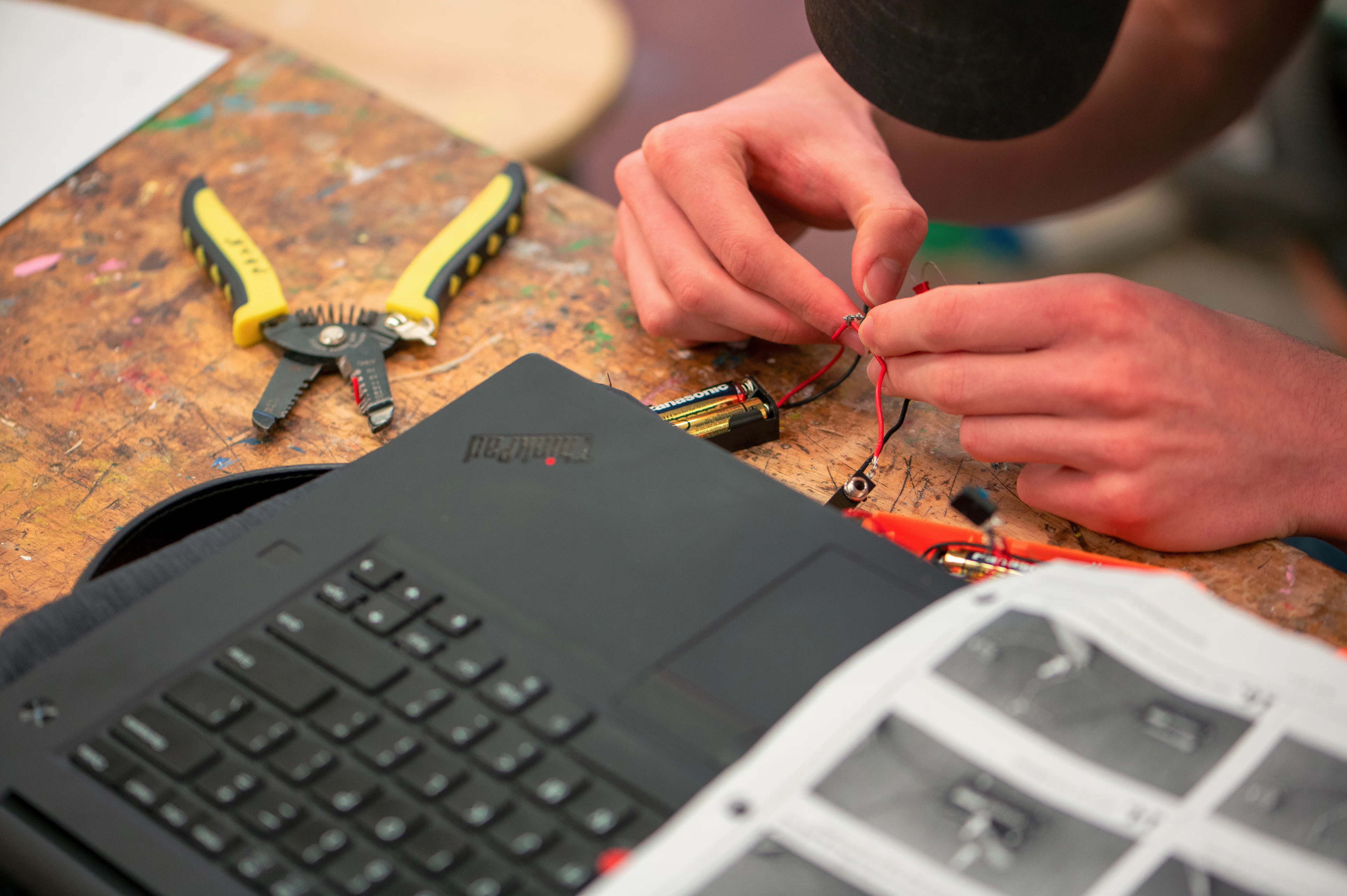 Mani che collegano componenti elettronici con gli attrezzi sul banco, accanto a un portatile