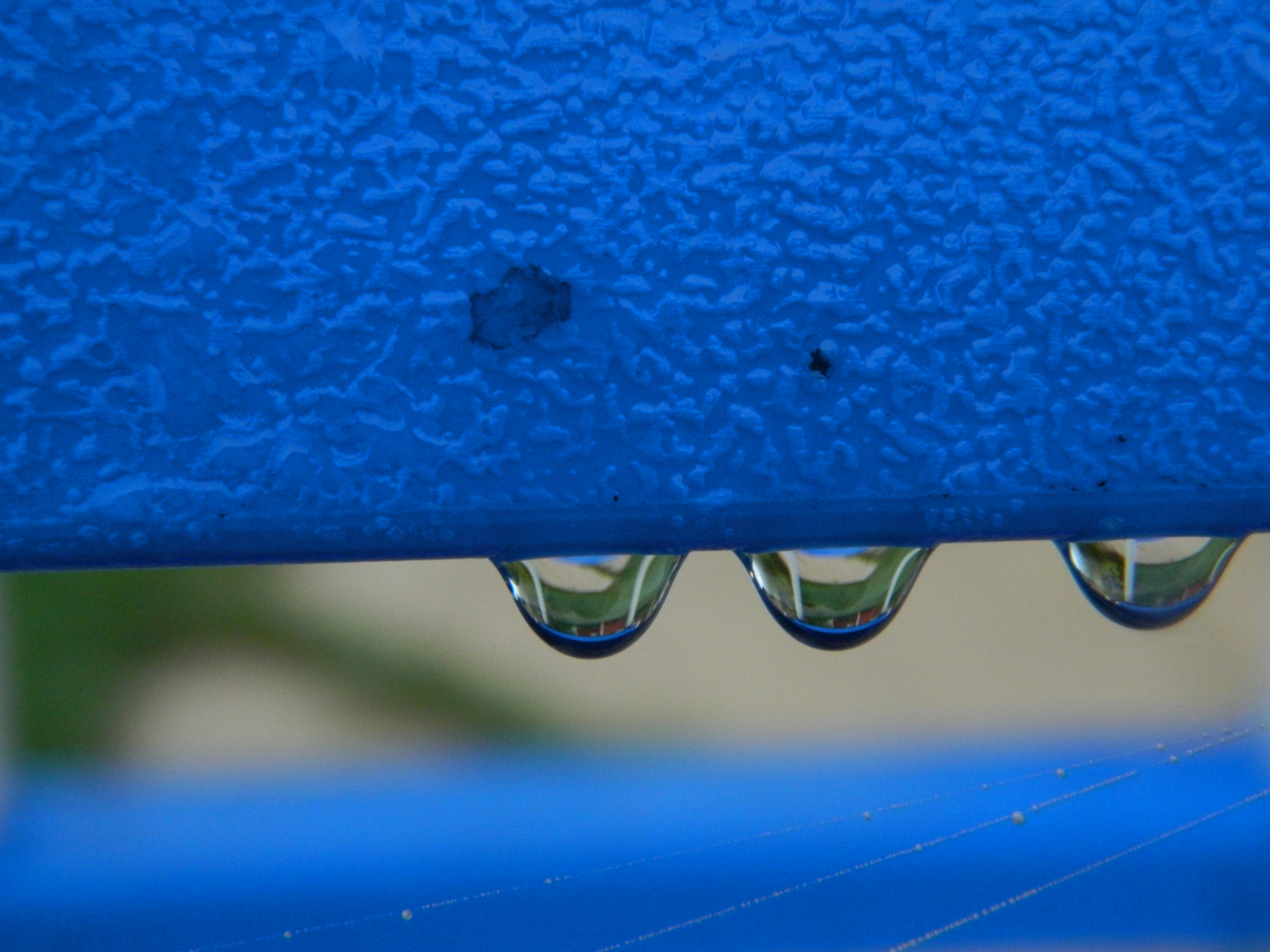 Water droplets hang from a blue surface.