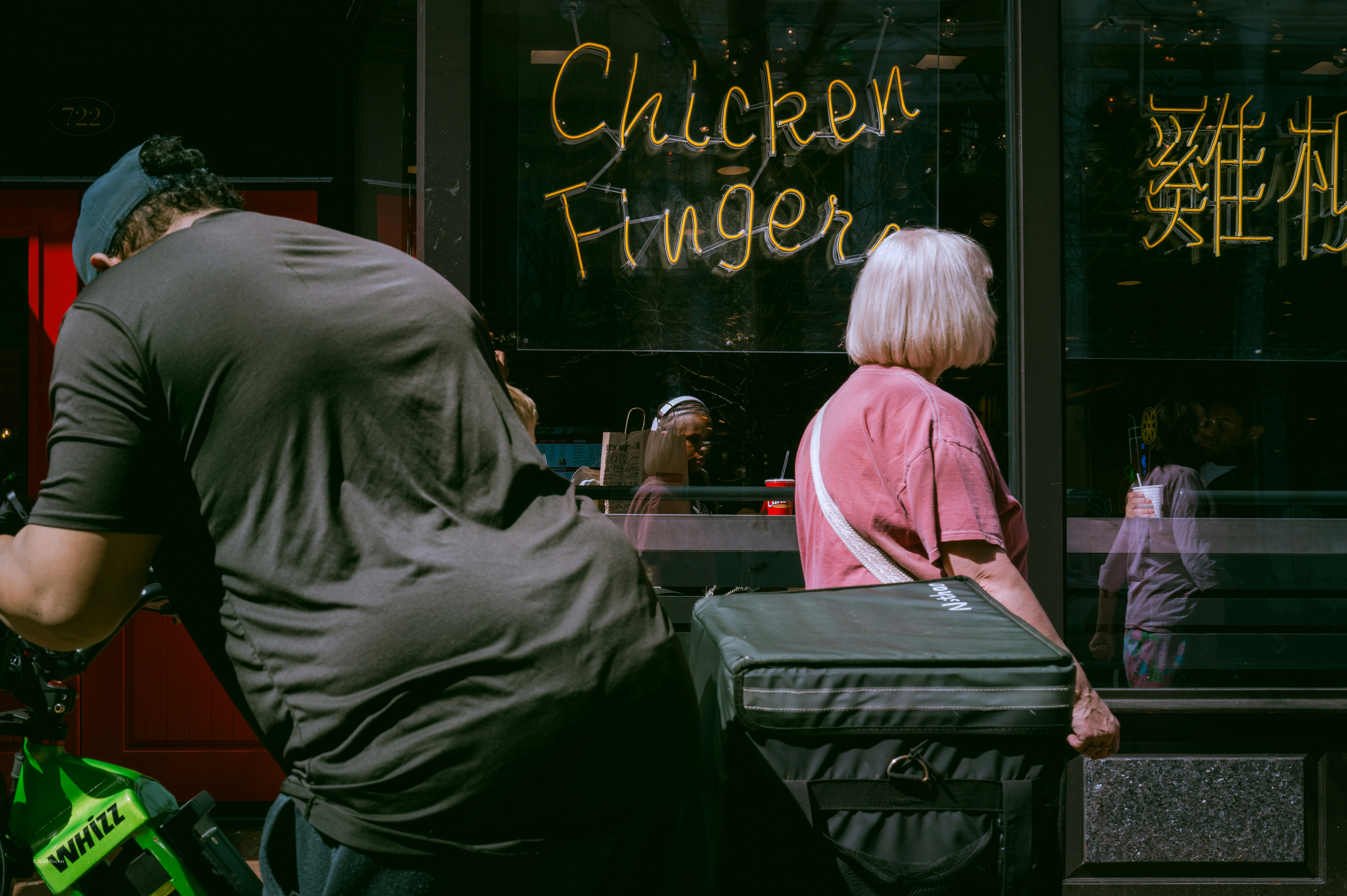 People walk past a storefront with "chicken finger" sign.