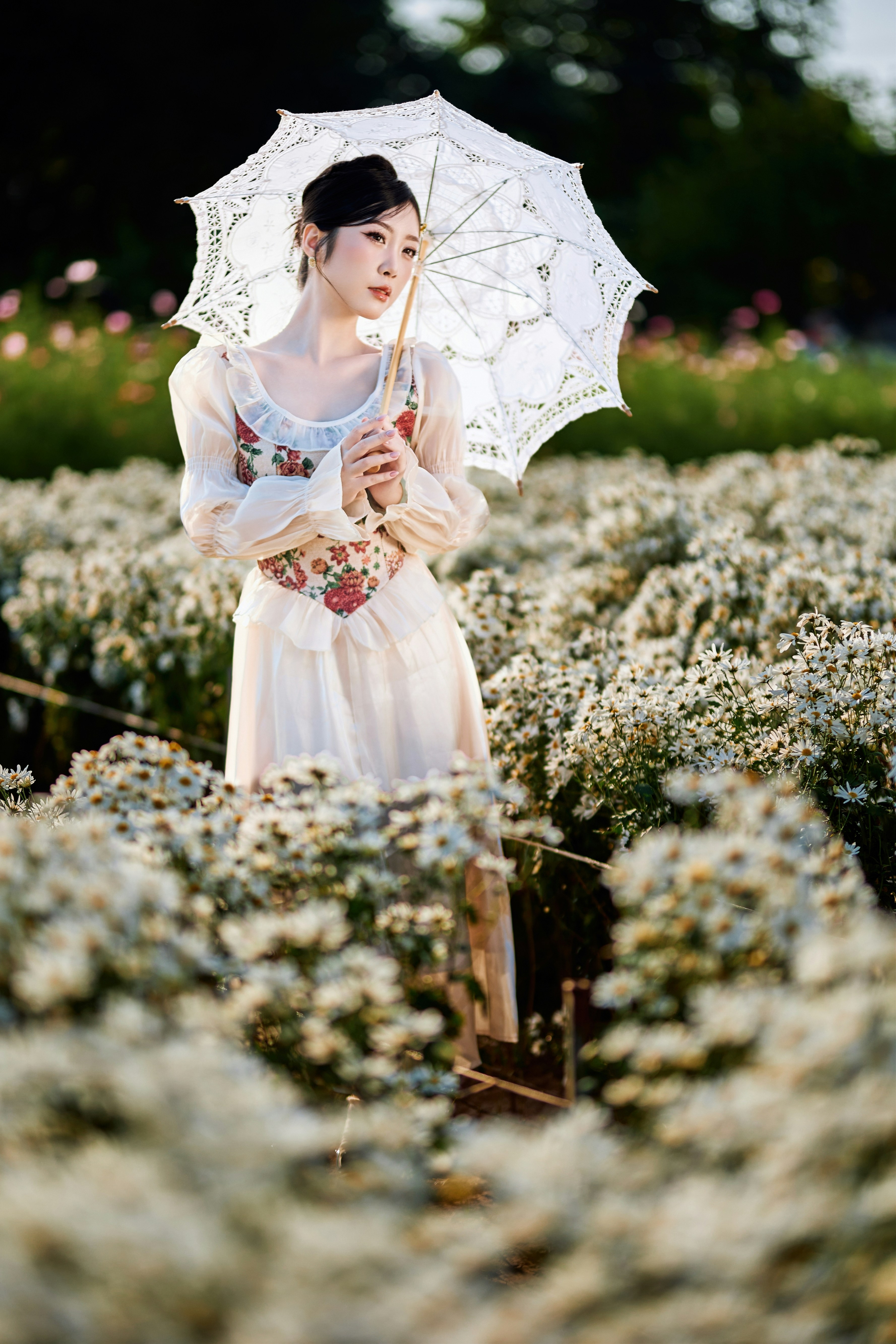 Woman in white dress holding umbrella in flower field