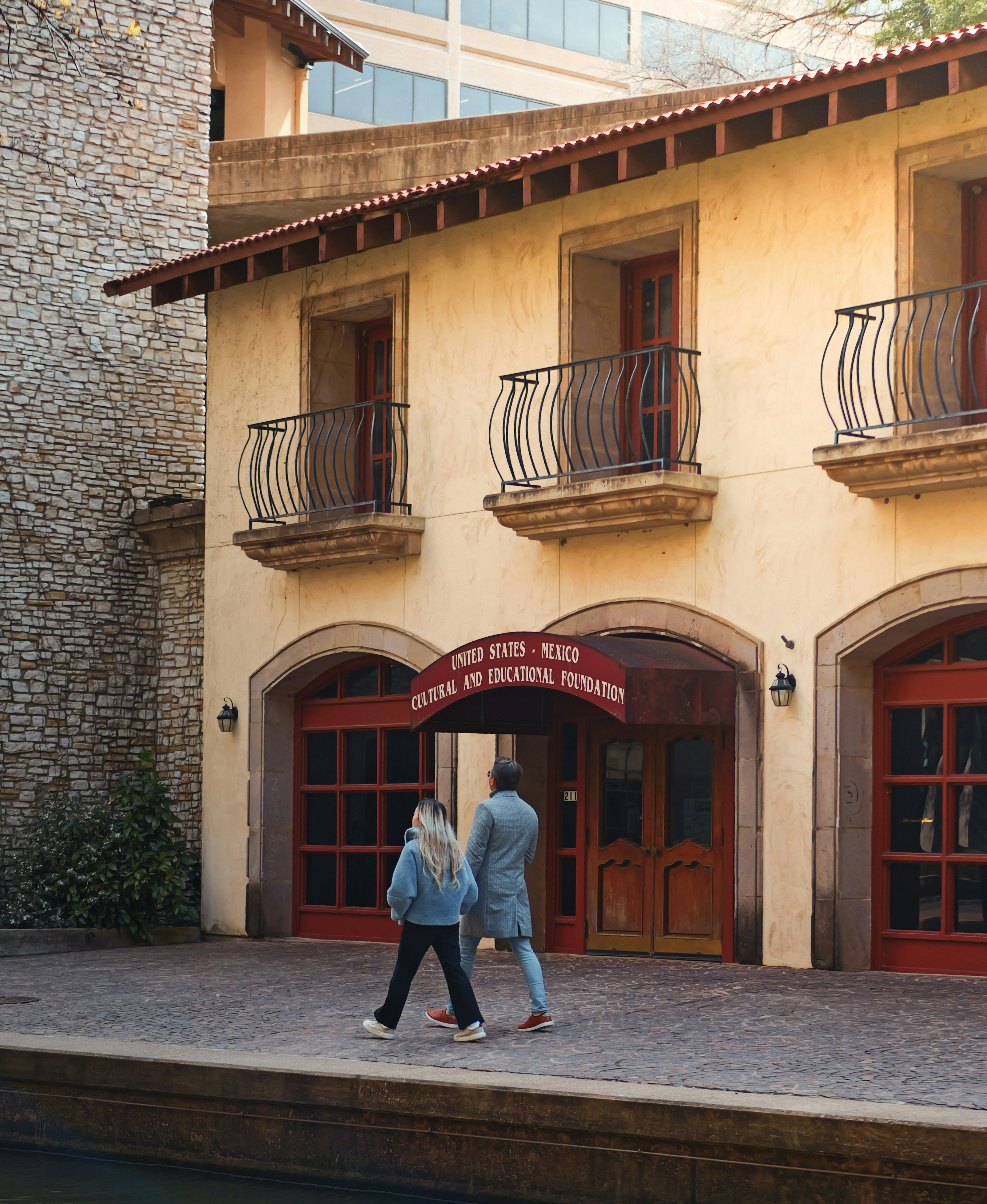 Deux personnes passent devant un bâtiment aux portes voûtées.