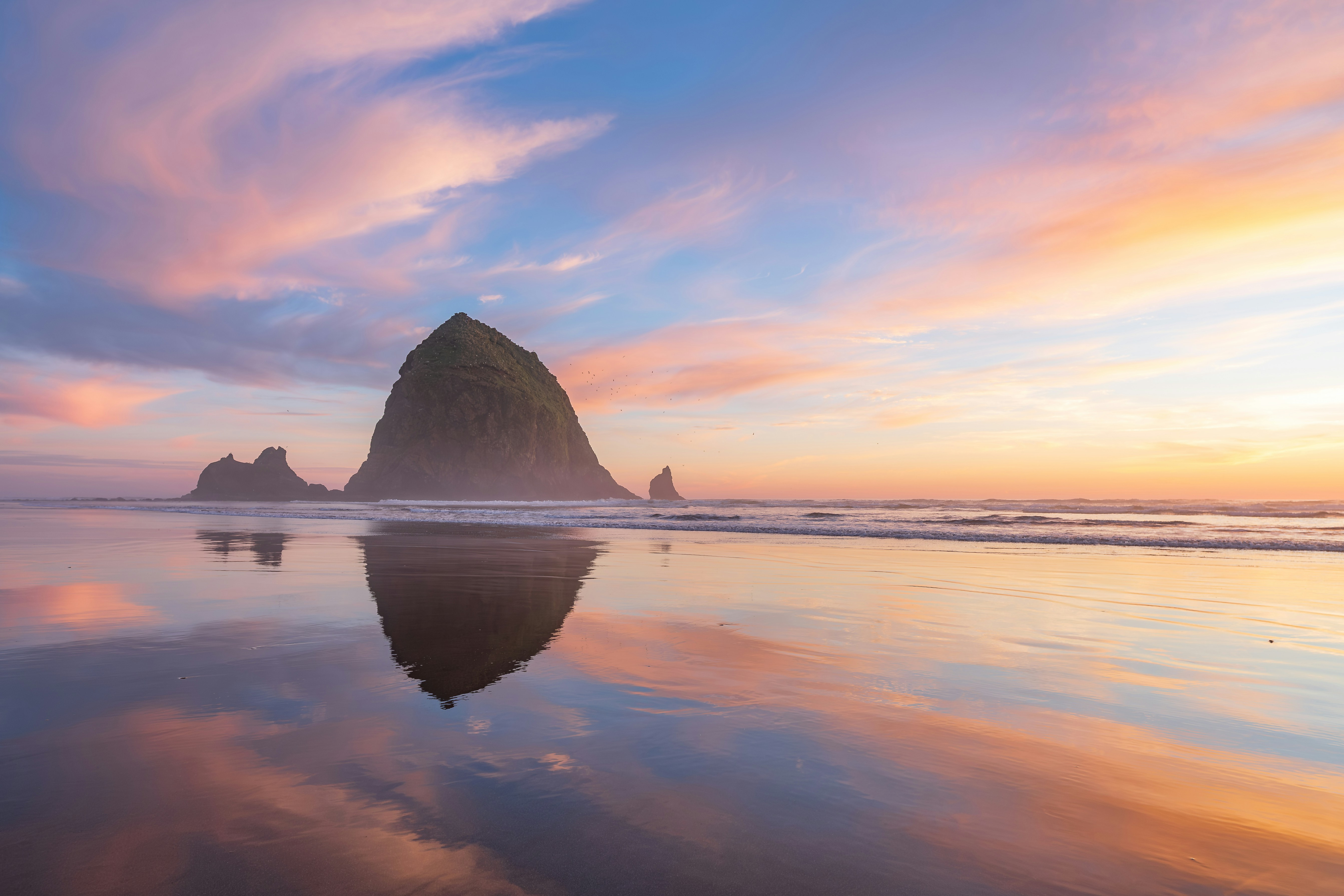Sea stack reflection on wet sand at sunset