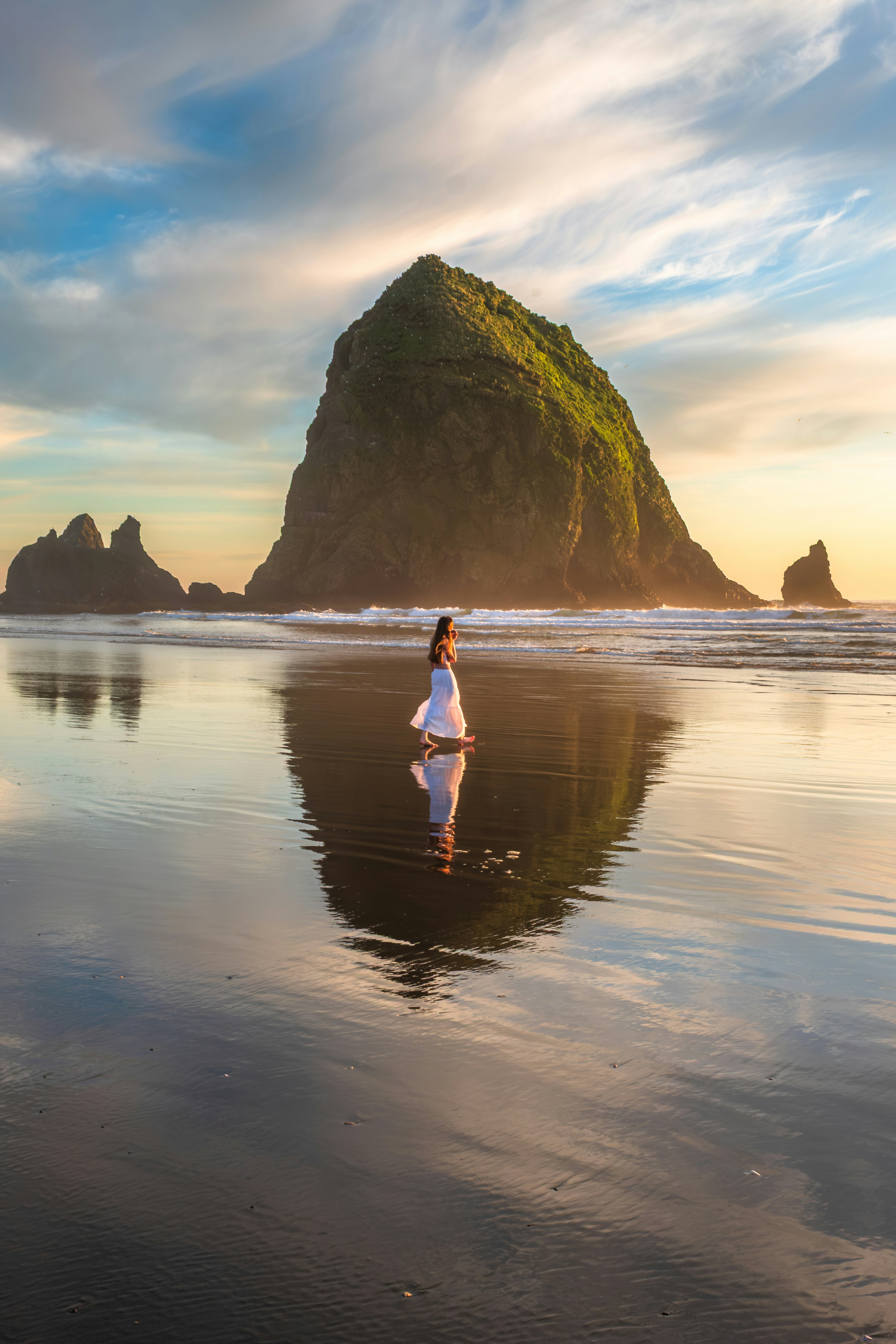 Woman in white dress on wet beach with rock formation