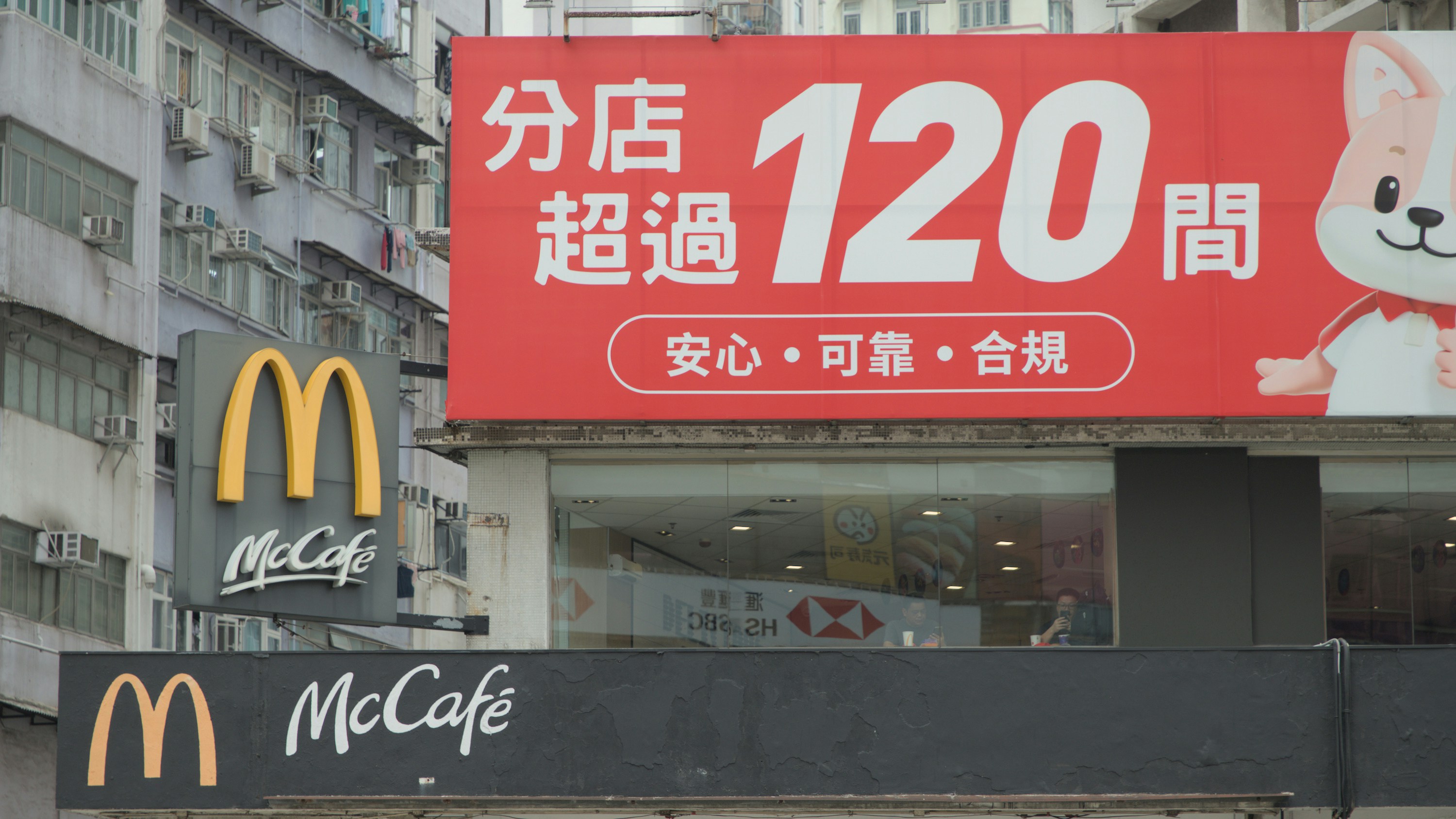 Costumers eating in a McDonalds restaurant which is located in the first floor in between the concrete jungle of Hong Kong.