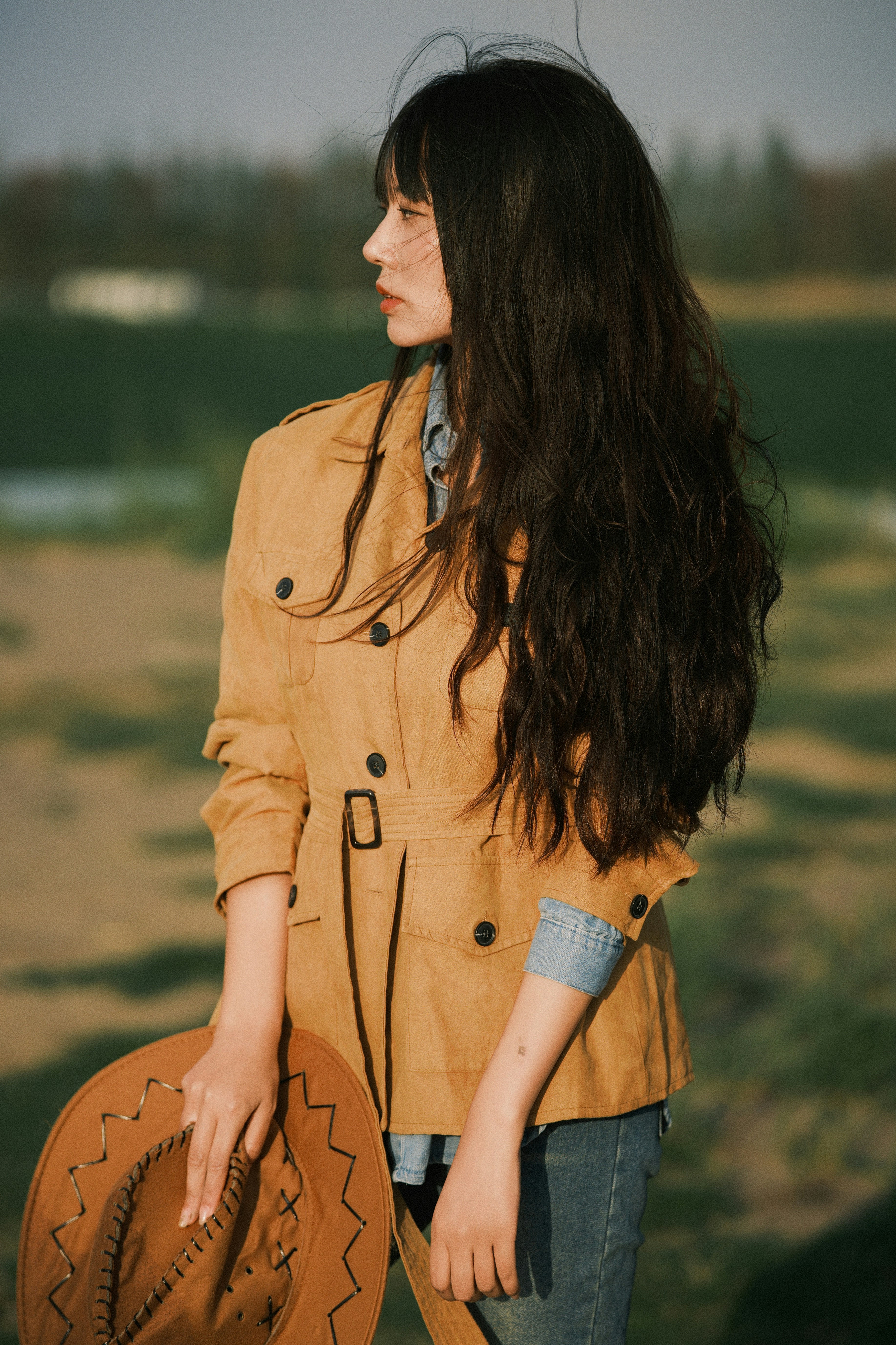 Woman in a tan jacket holding a cowboy hat outdoors