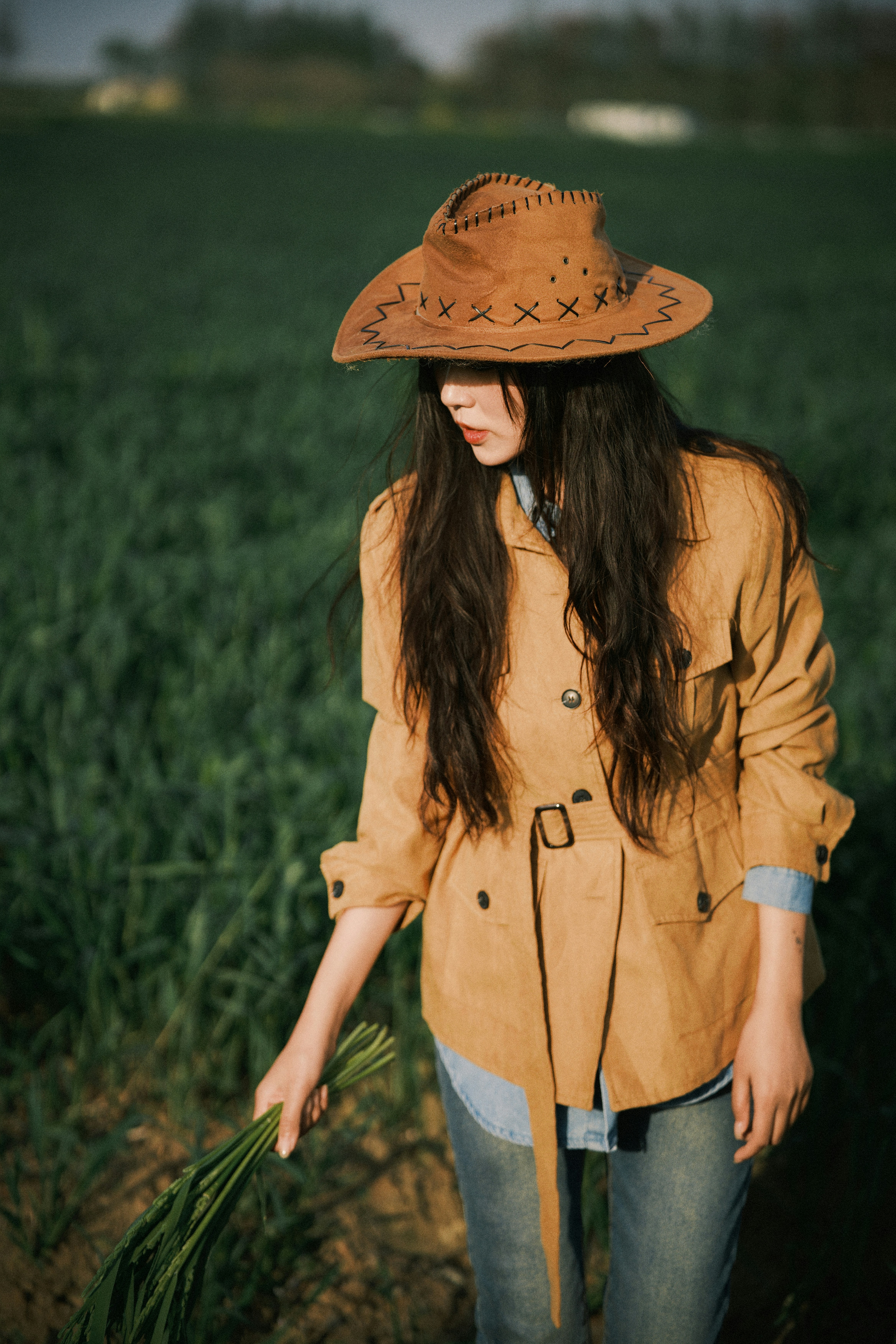 Woman in cowboy hat holding green stalks in field