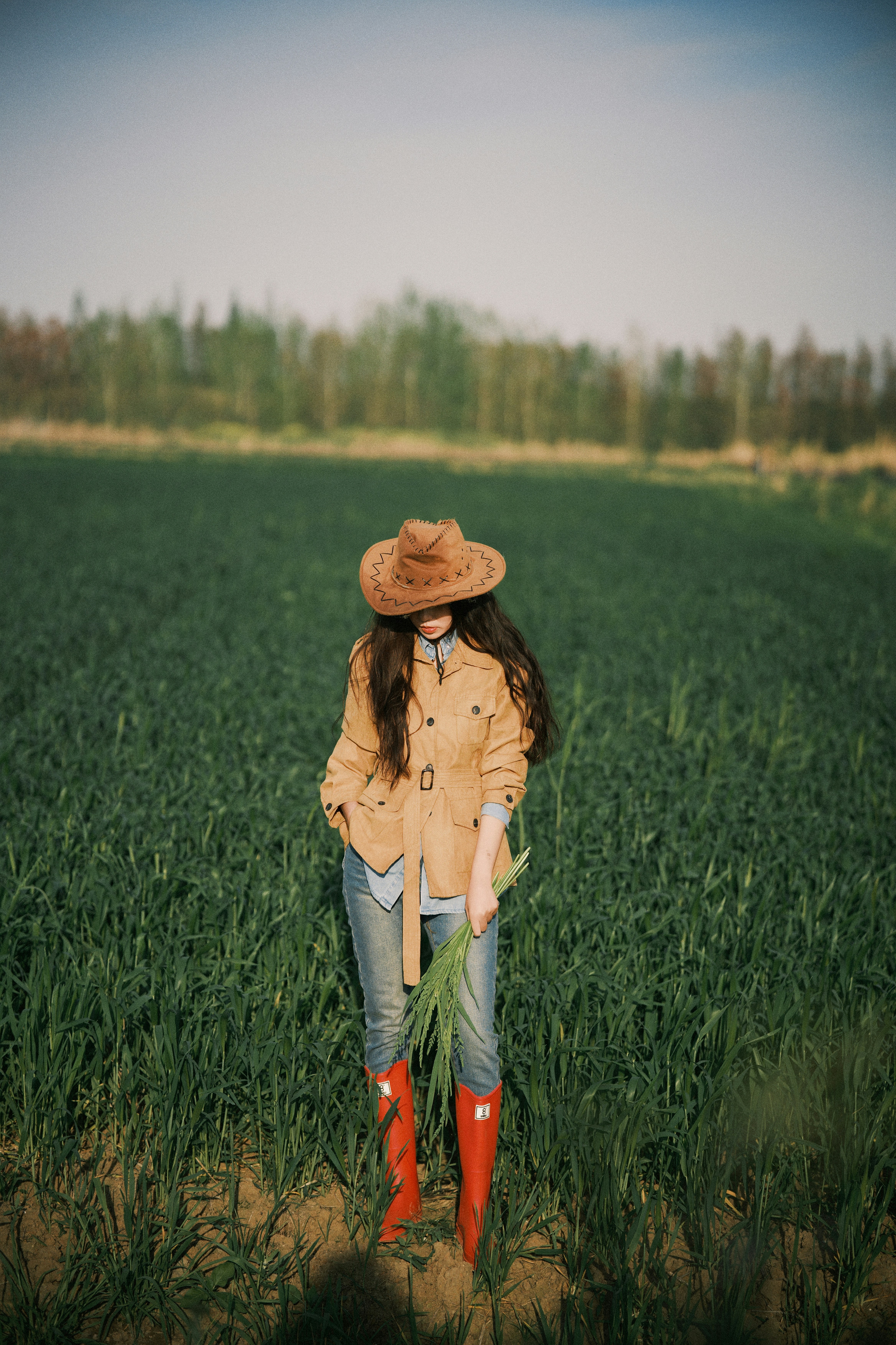 Woman in cowboy hat stands in a green field.