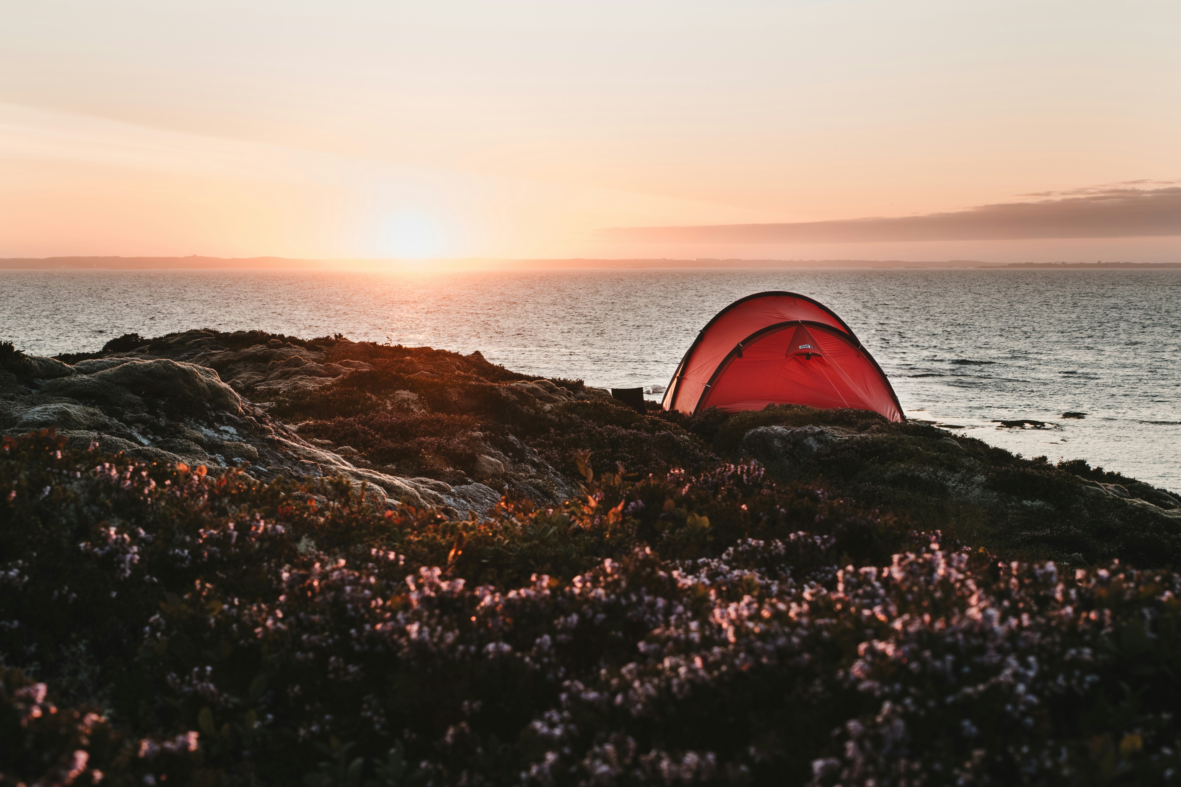Rotes Zelt auf einem Hügel mit Blick auf den Ozean bei Sonnenuntergang