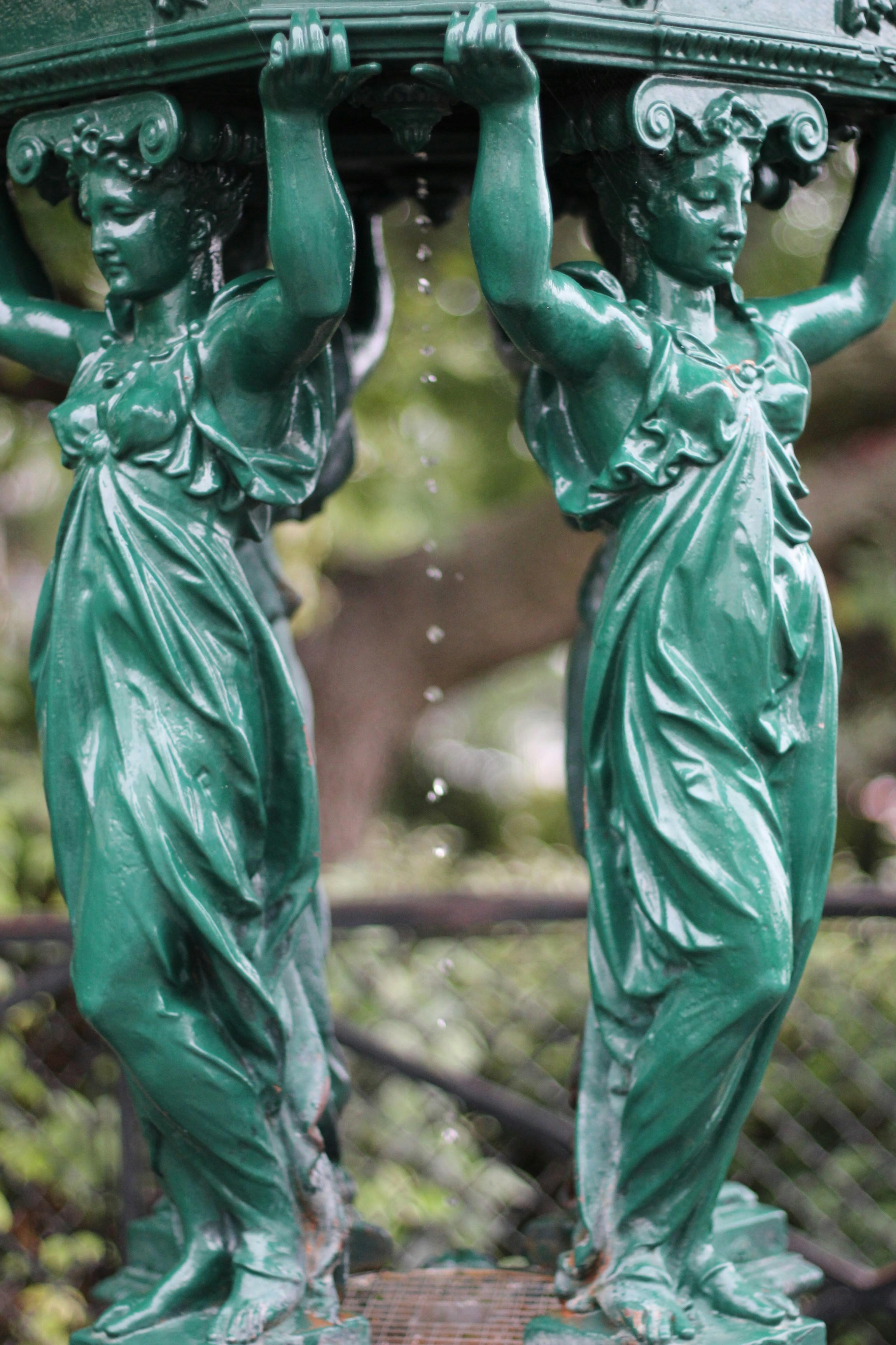Two green statues holding up a fountain