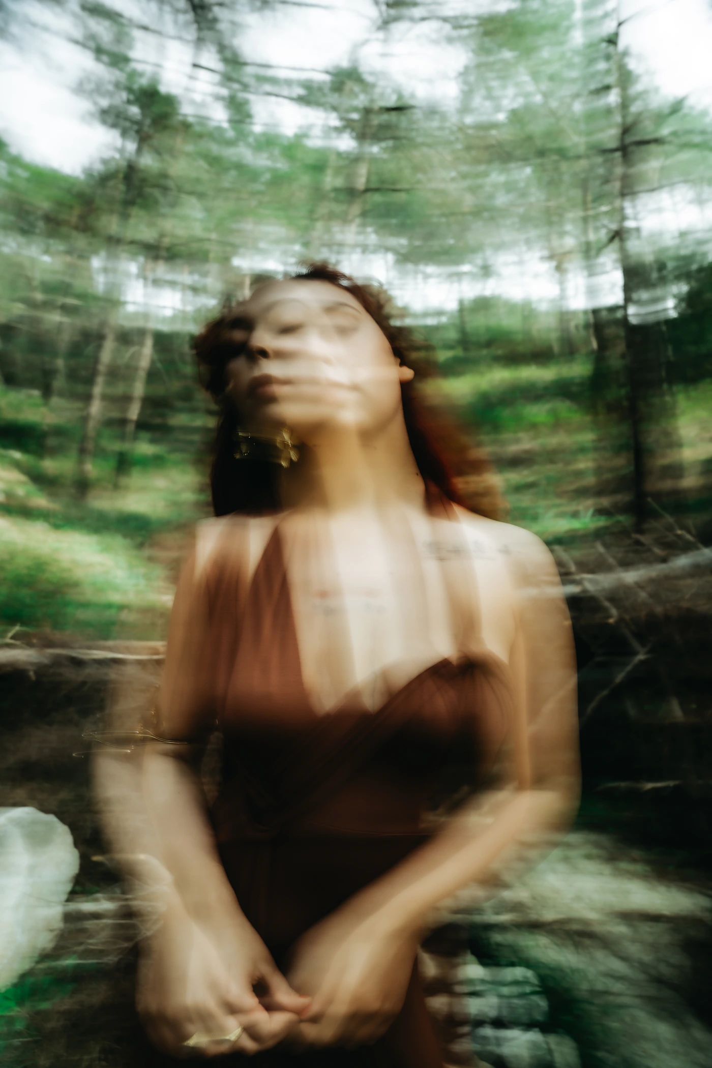 Blurred dreamy image of a woman in a flowing dress in a forest with soft ethereal fine art quality and film-like tones