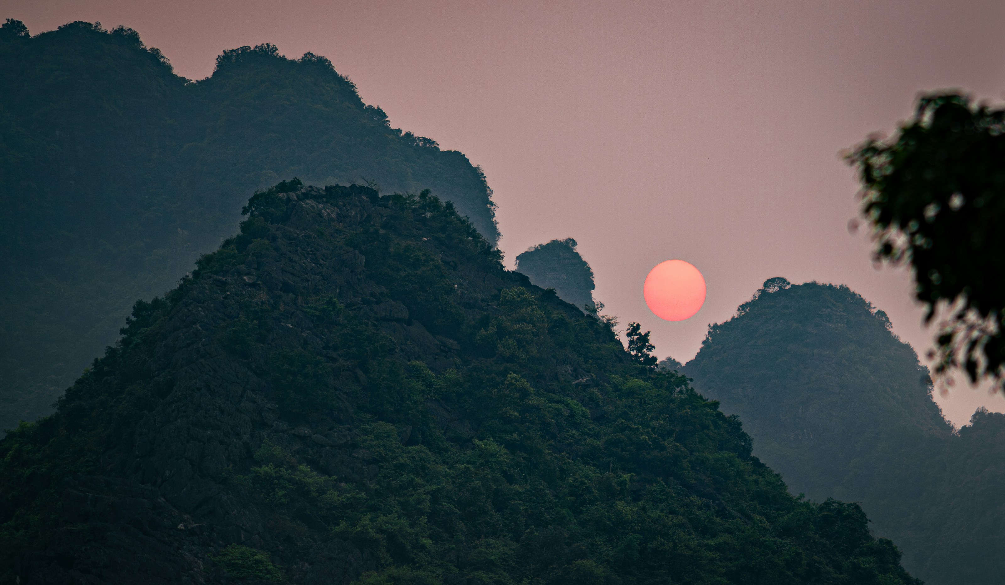 Pink sun setting behind misty mountains at dusk